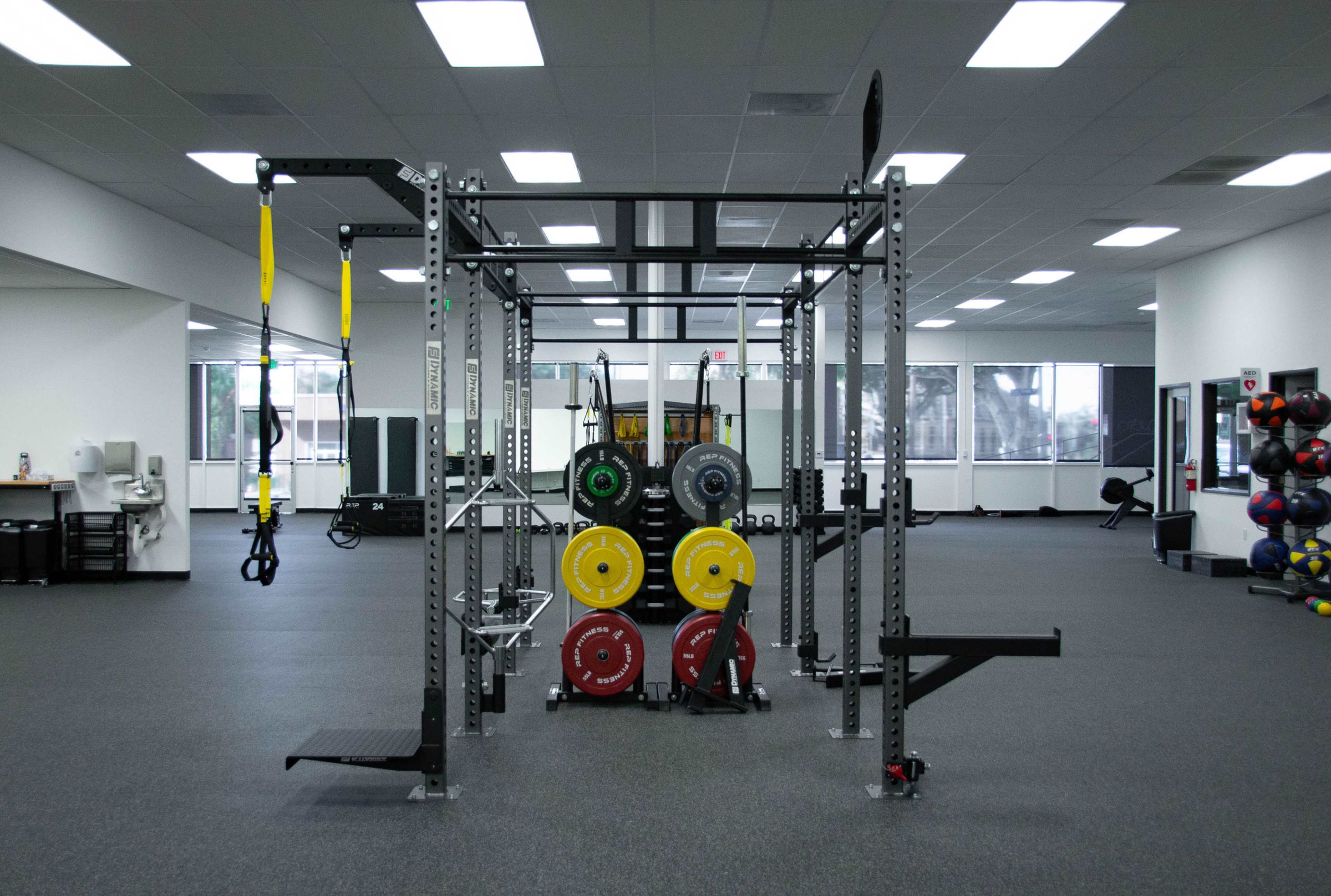 A fitness facility features a multi-functional gym rig with weight plates and exercise bands organized in a spacious workout area.