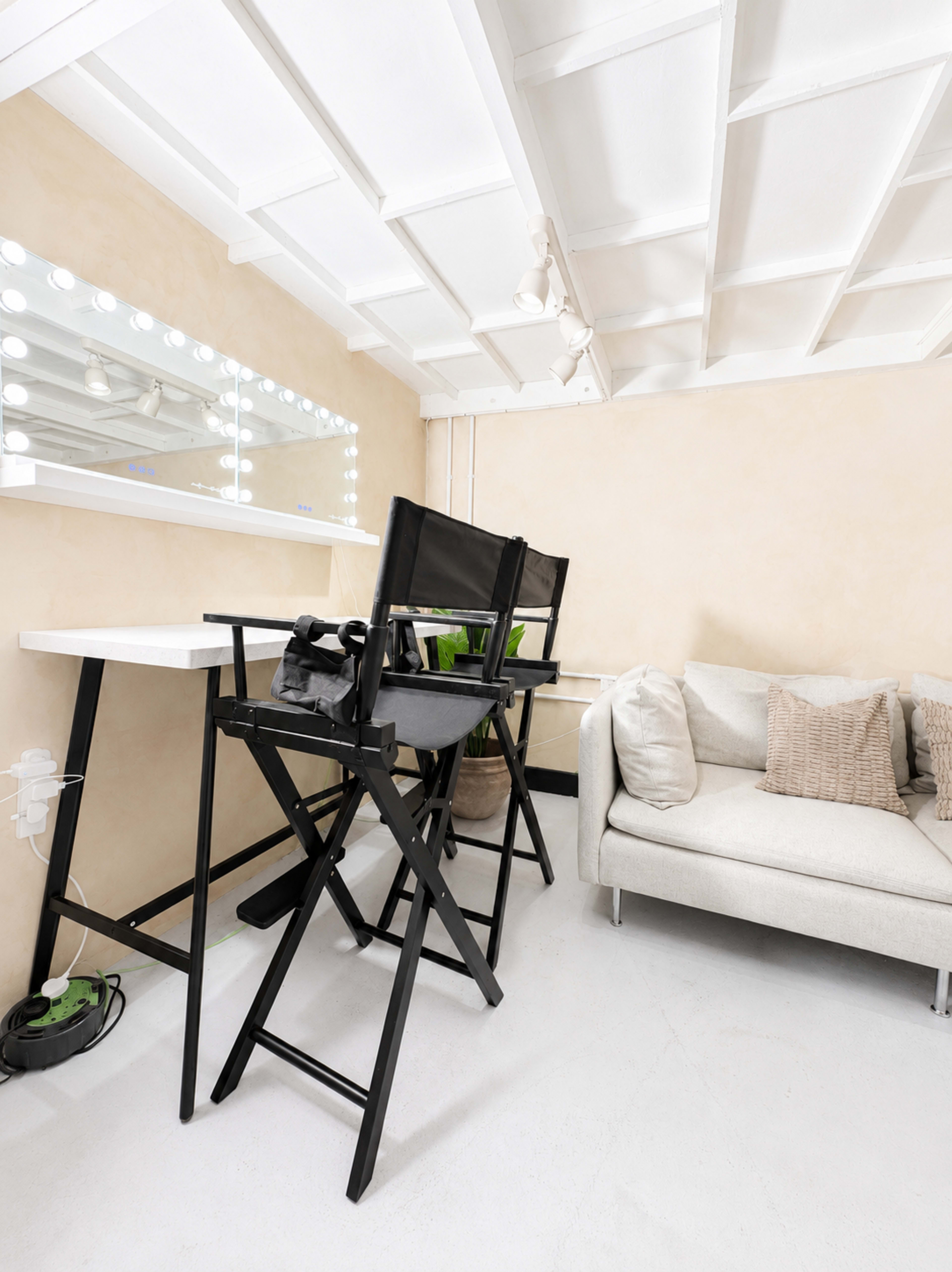 The image shows a modern, well-lit room featuring a pair of black director's chairs next to a white table and a light-colored sofa against a beige wall.