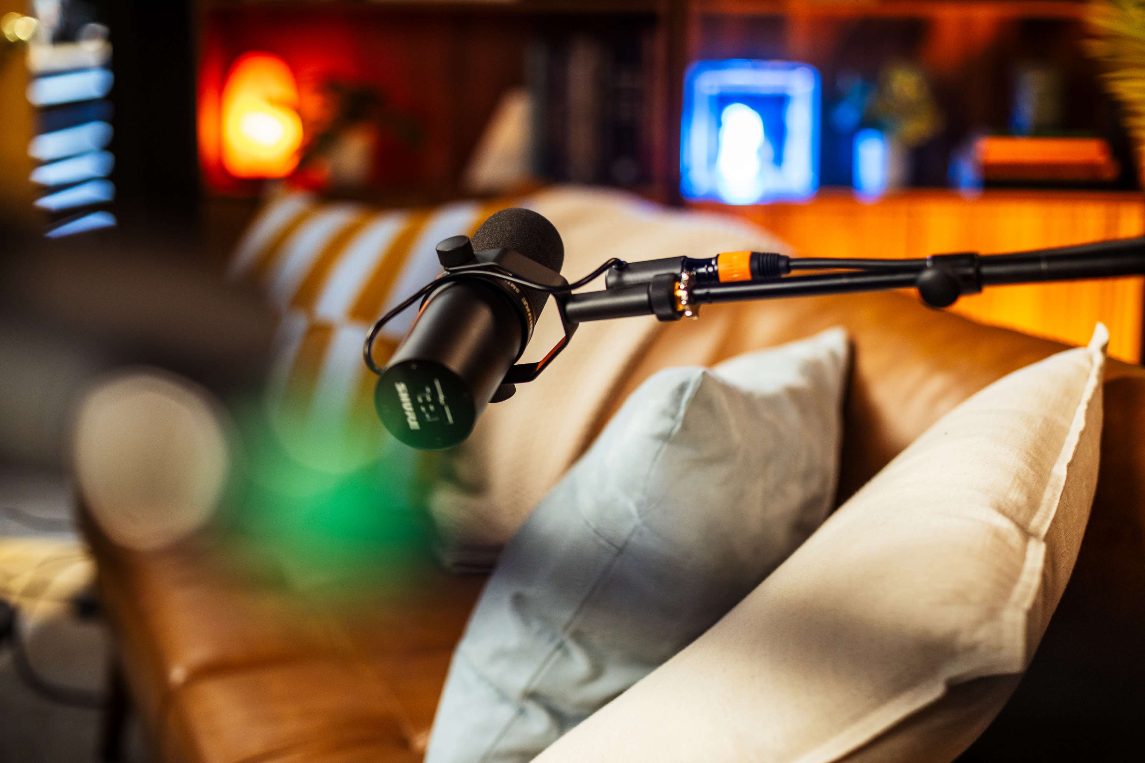 A microphone is positioned on a stand beside a couch adorned with decorative pillows in a well-lit room.