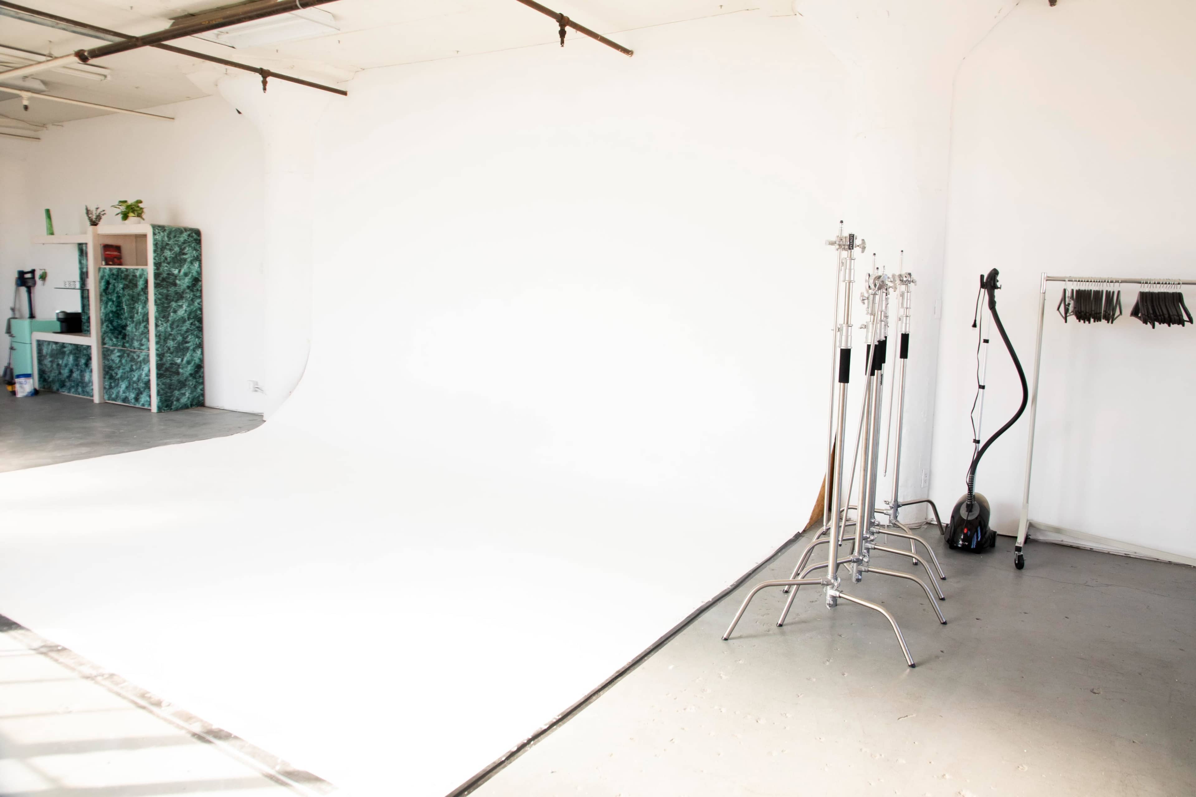 A spacious studio with a white backdrop, photography stands, and a clothing rack on the right.