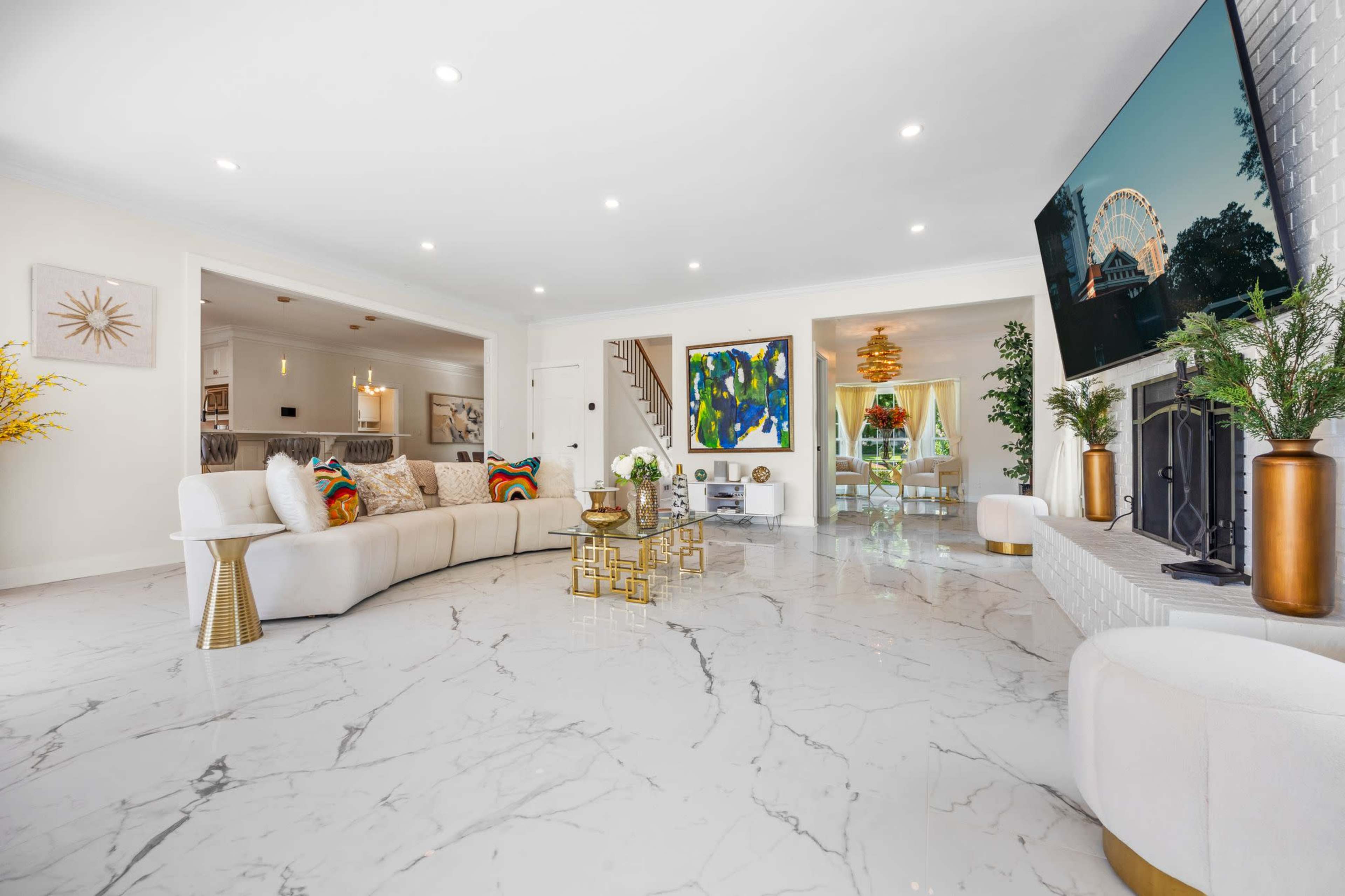 A spacious living room features a large sectional sofa, a coffee table, and a fireplace, with modern decor and white marble flooring.