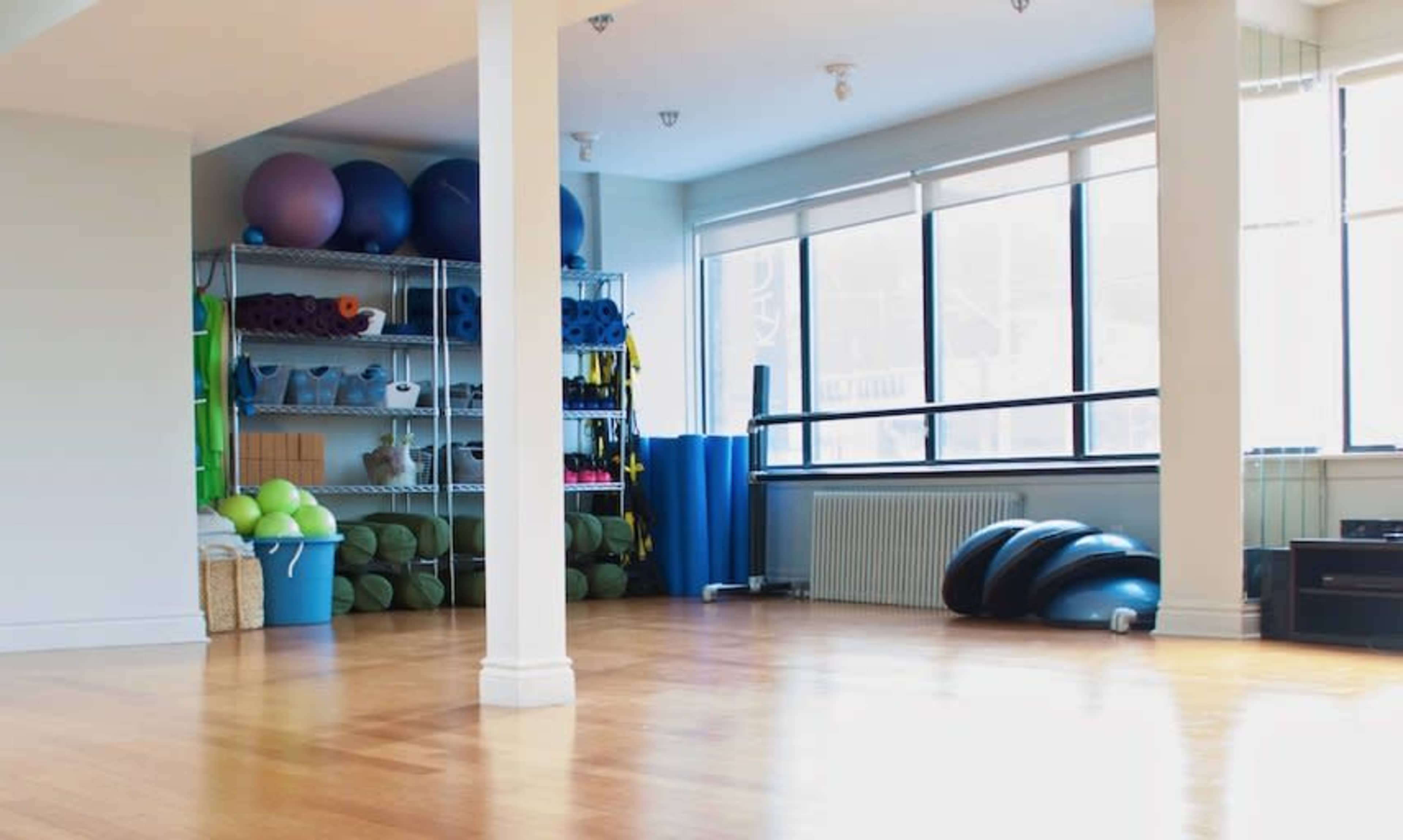 A bright, spacious fitness studio with exercise equipment neatly arranged on shelves and the floor.