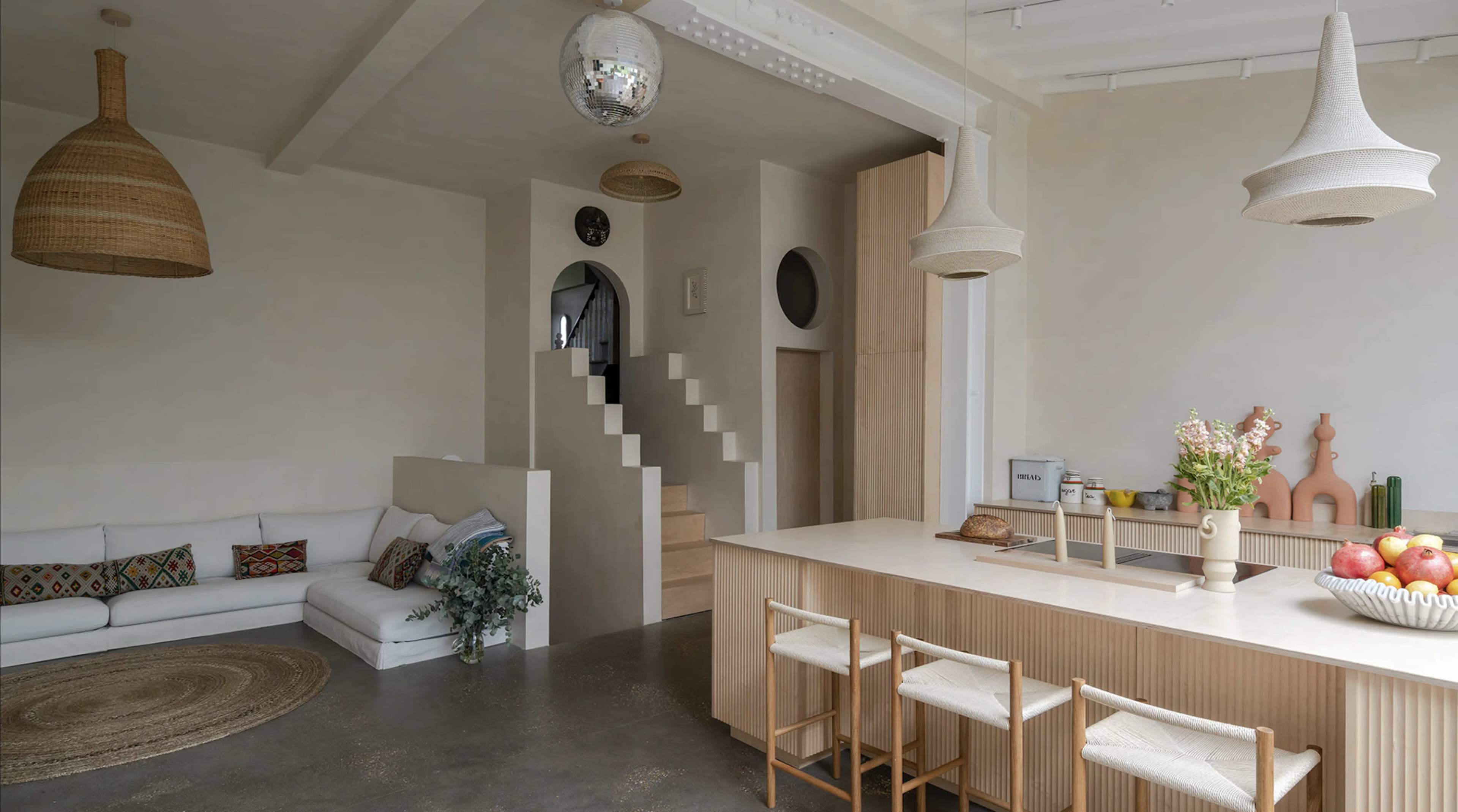 A modern, open-concept living space featuring a kitchen island with seating, a staircase, and a cozy sitting area with a circular rug.