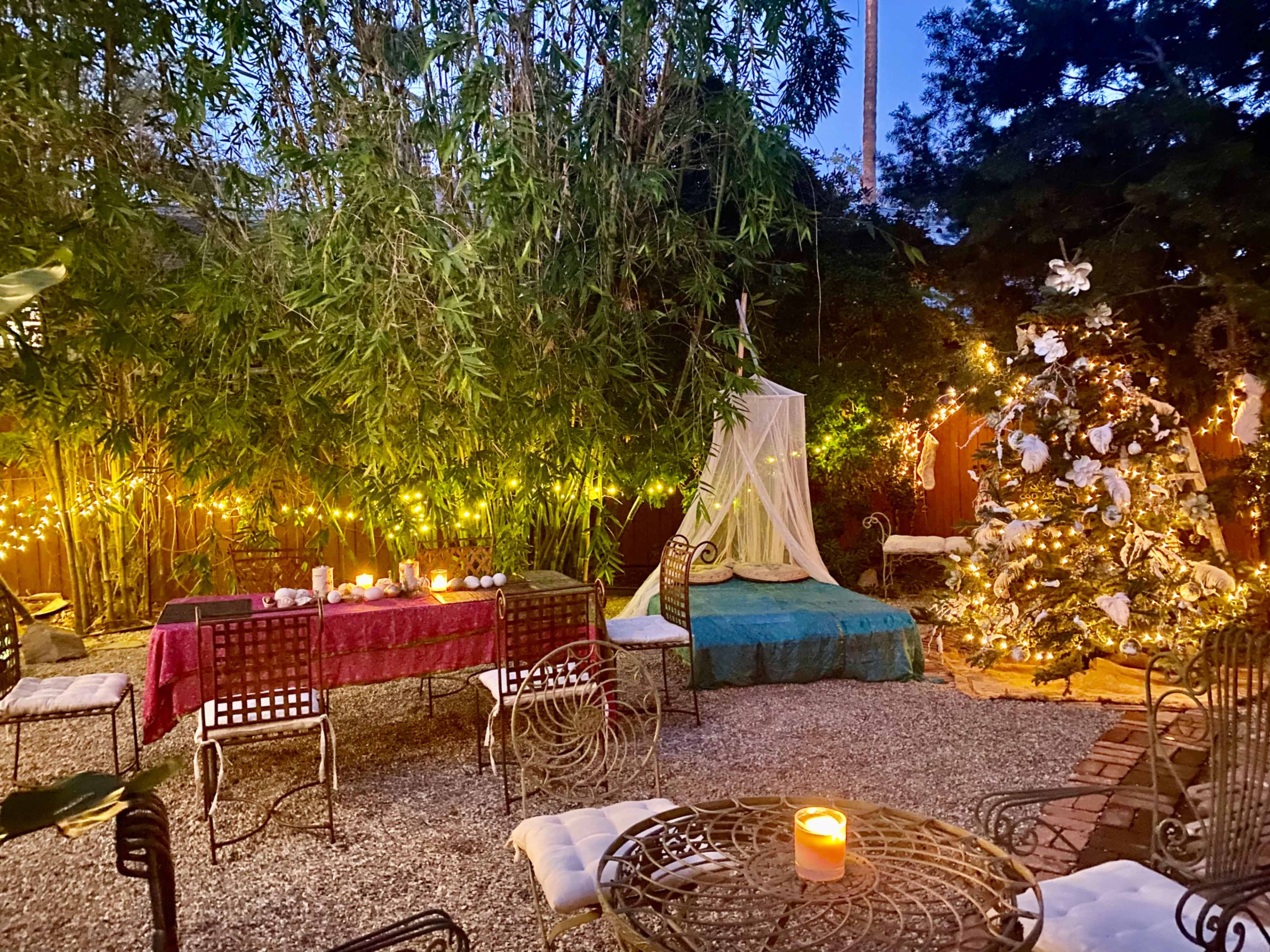 The outdoor garden features a table with chairs, a decorated Christmas tree with lights, and a cozy seating area draped with fabric.
