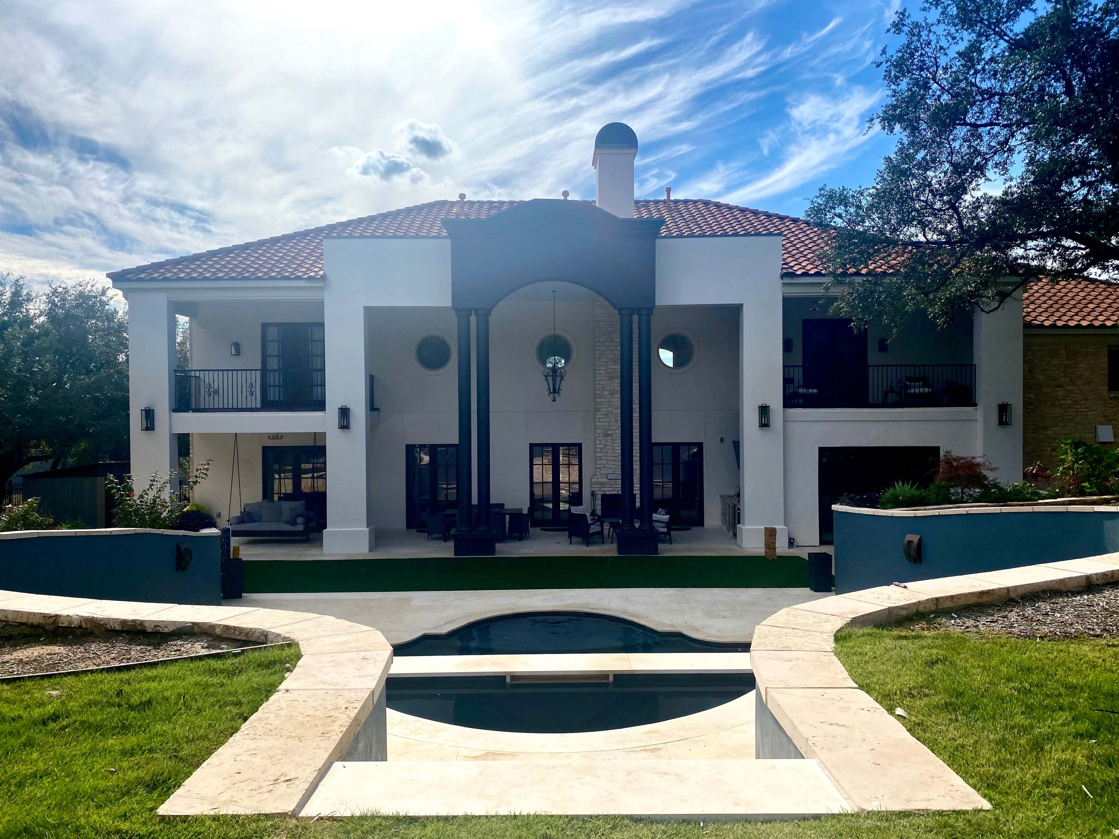 The image shows a large two-story house with a tile roof, surrounded by greenery and featuring a pool in the foreground.