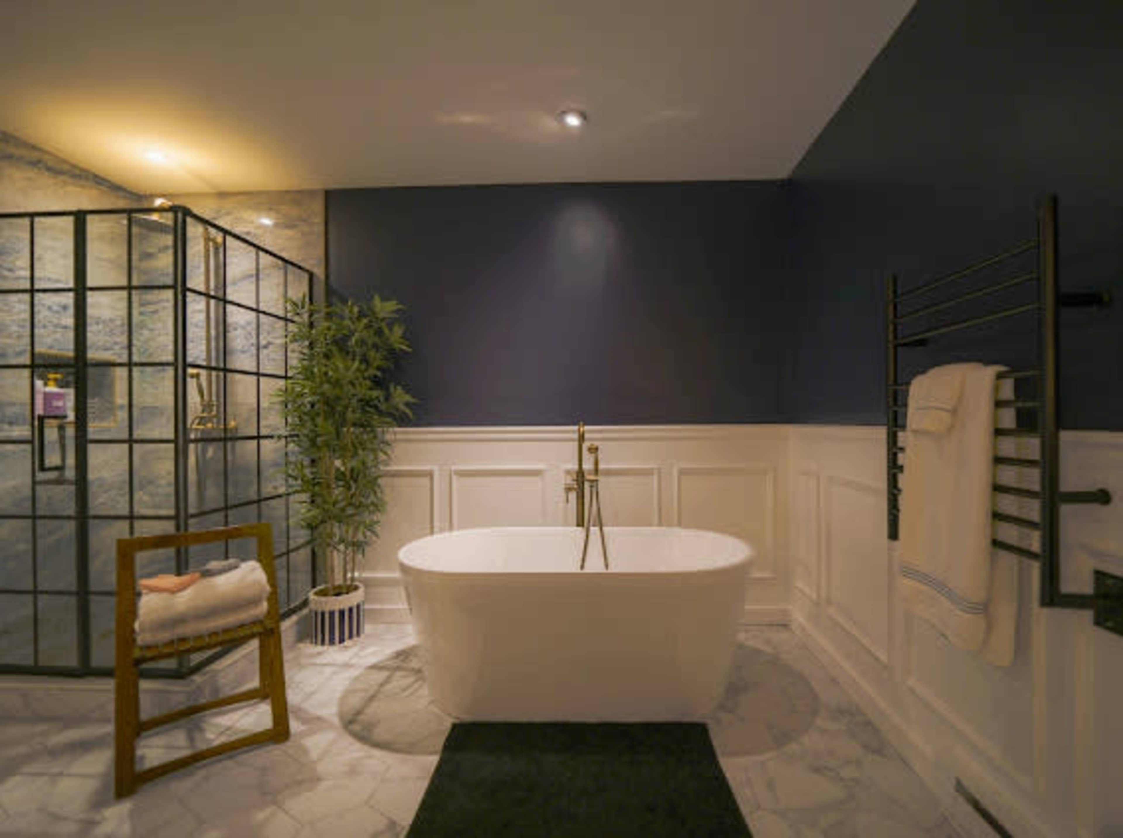 The image shows a modern bathroom featuring a freestanding white bathtub, a glass shower enclosure, and a decorative plant beside a wooden chair.