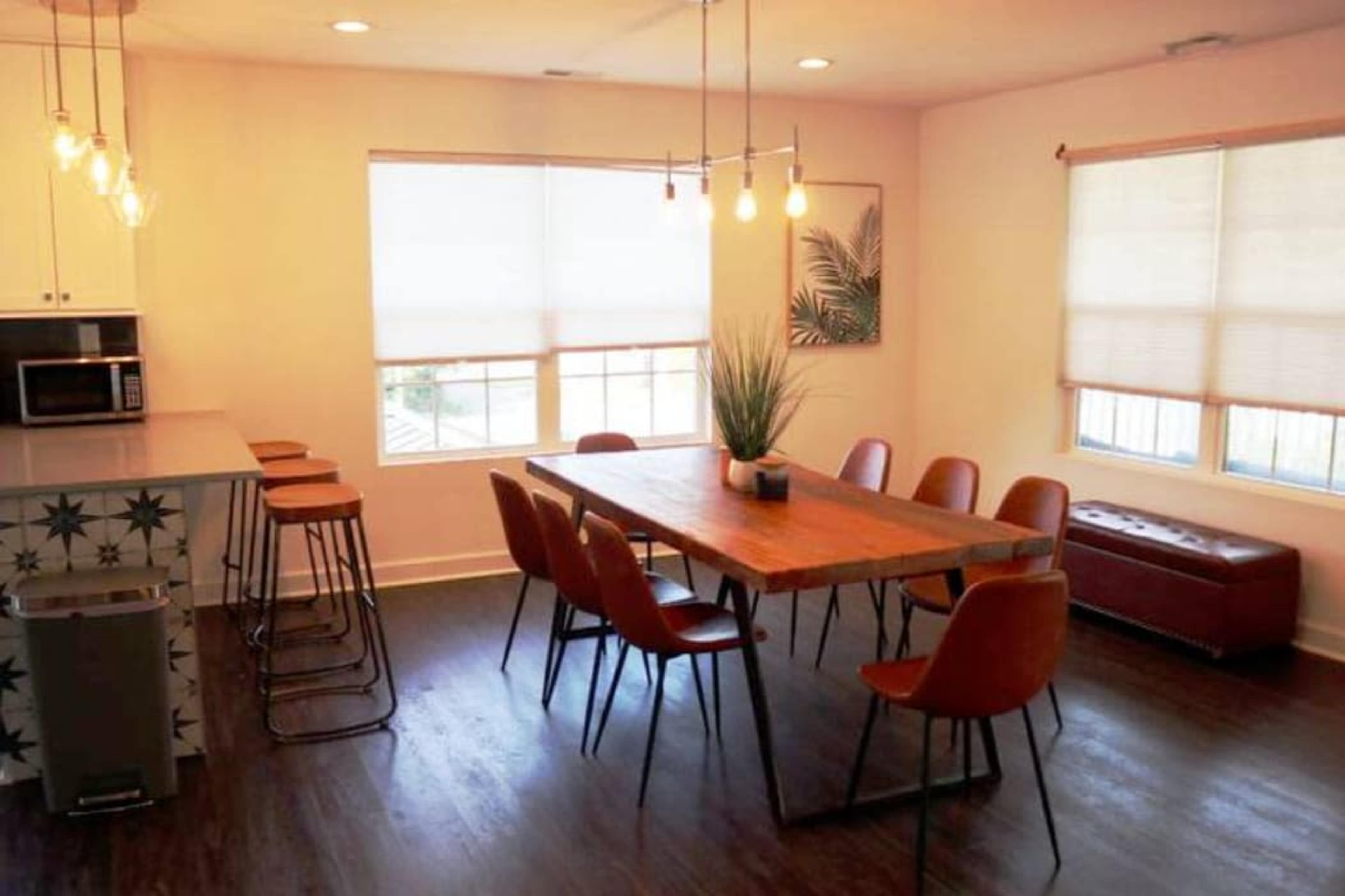 A modern dining area featuring a wooden table surrounded by eight chairs, with large windows and pendant lighting illuminating the space.