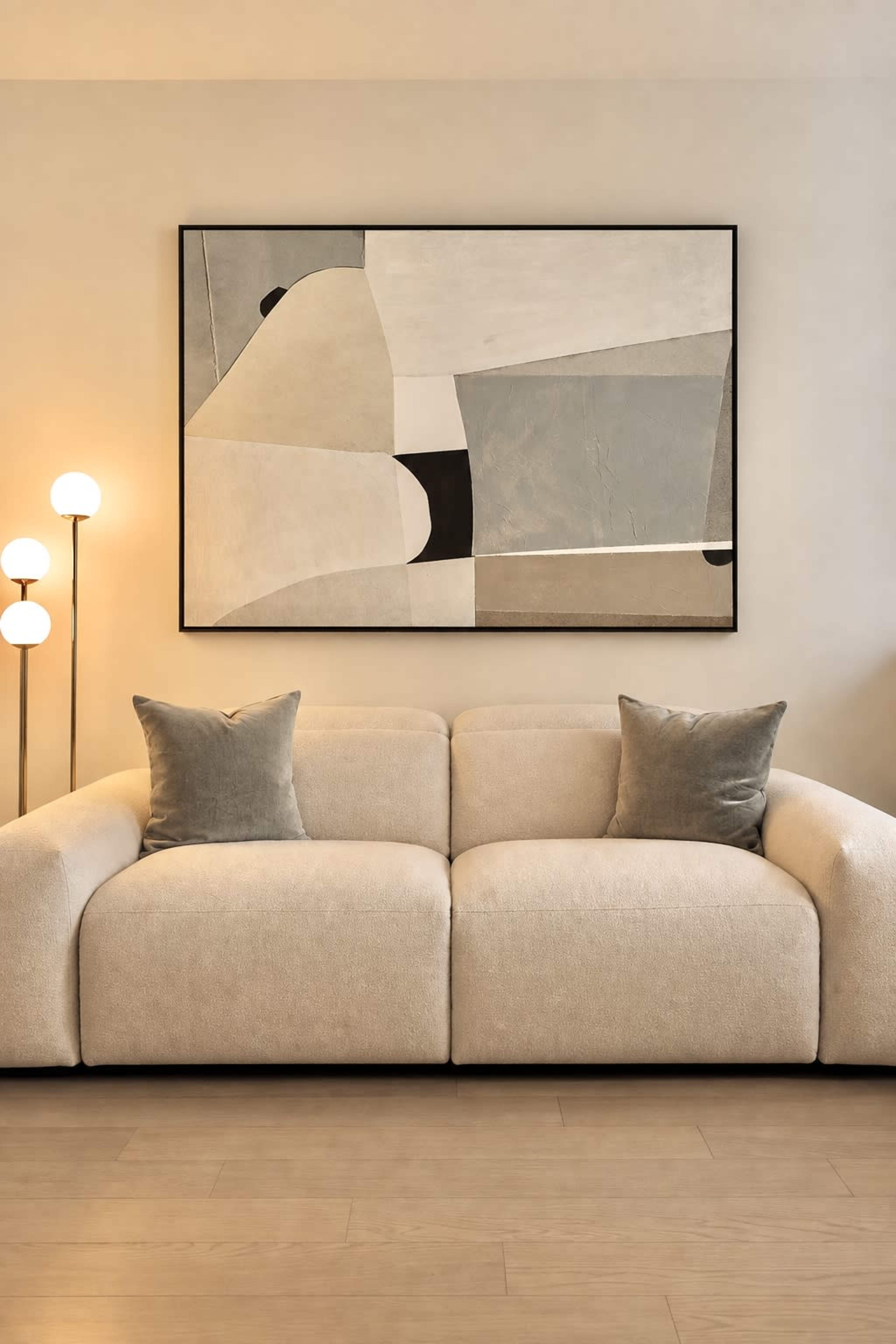 A modern living room features a beige sofa with two decorative pillows and a large abstract painting on the wall behind it, alongside a standing lamp.