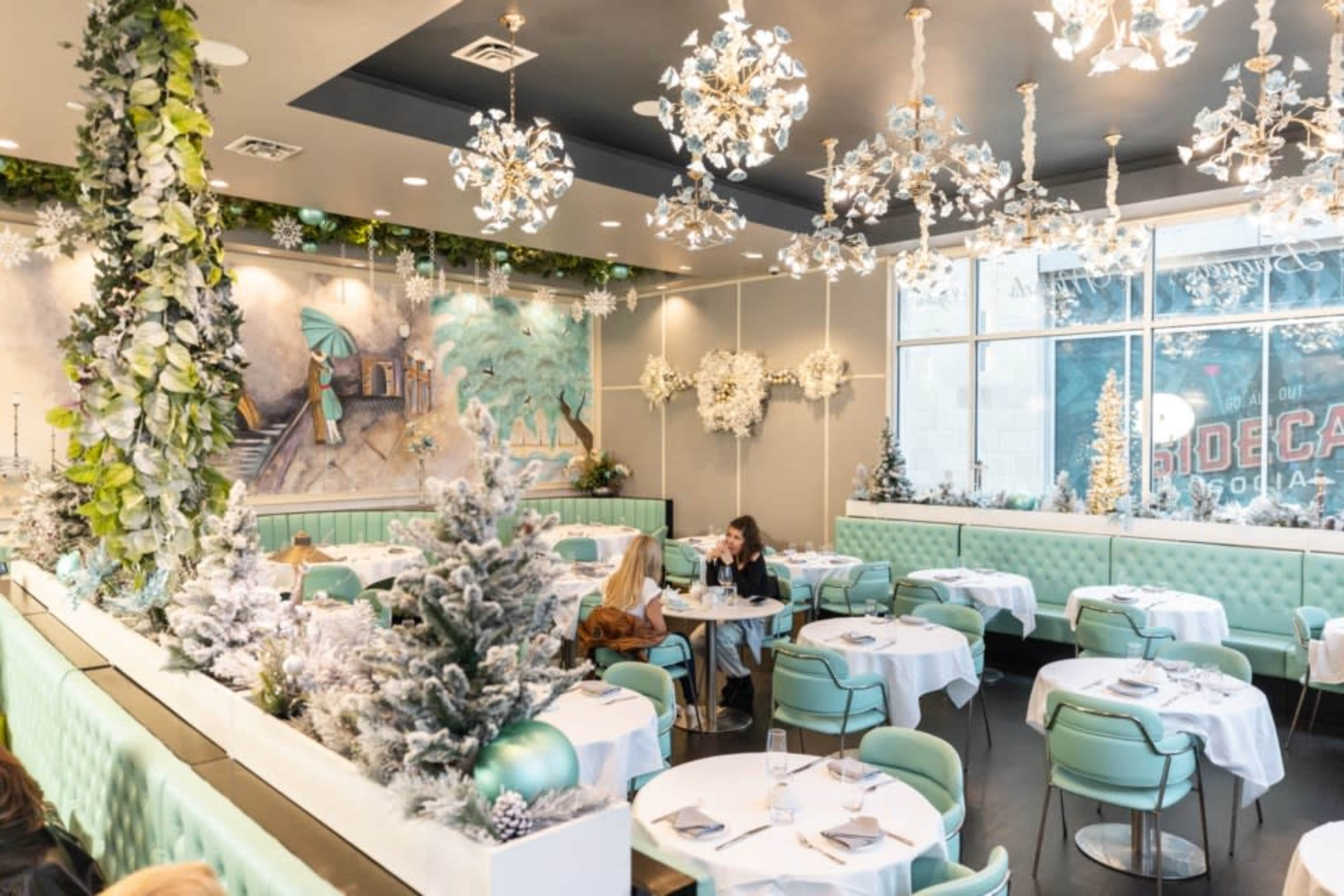 A modern dining area is adorned with winter-themed decorations, featuring green upholstered seating and snowy centerpieces.