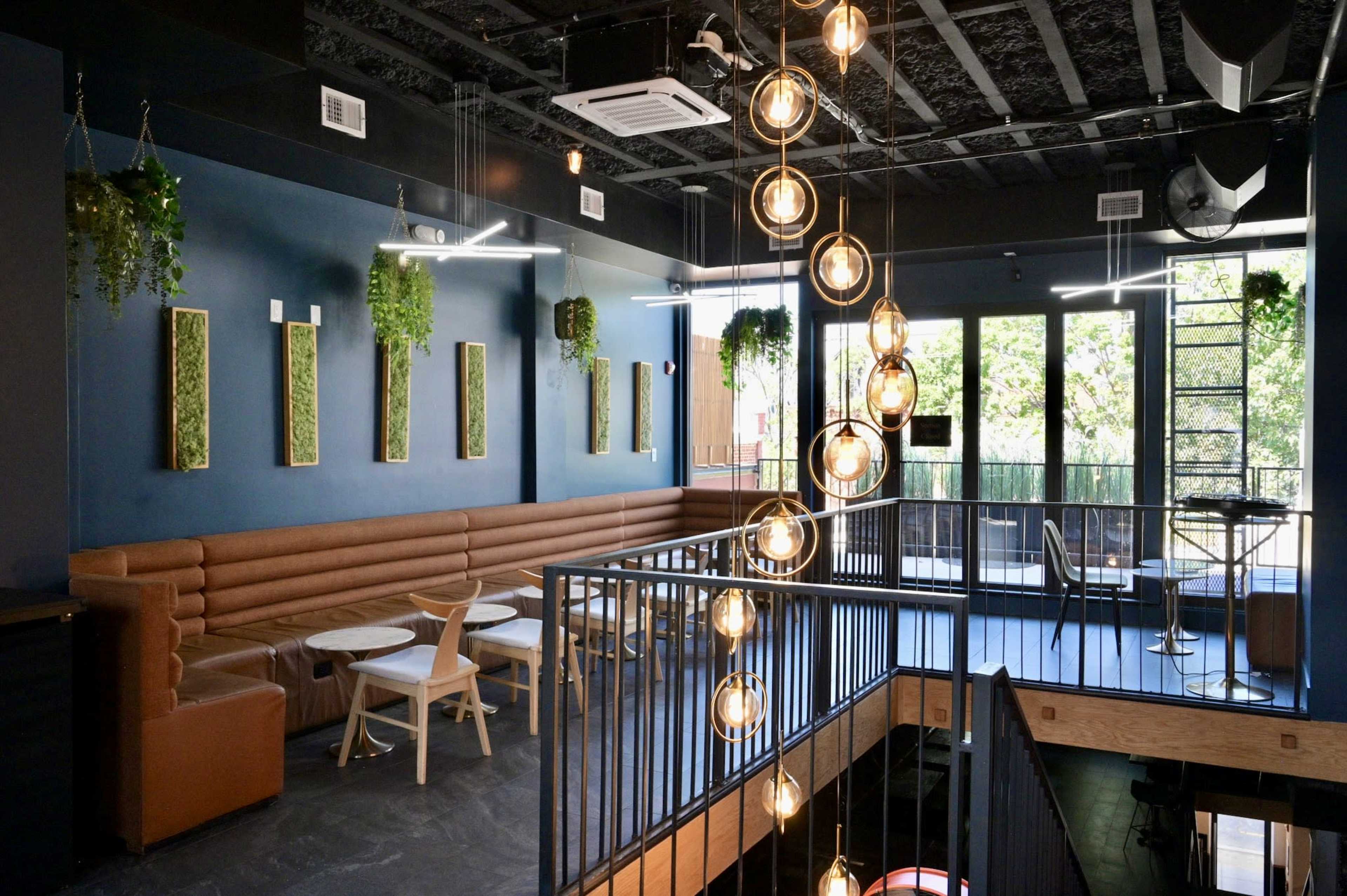 The image shows a modern café interior with a brown leather seating area, circular tables, and industrial-style lighting hanging from the ceiling.