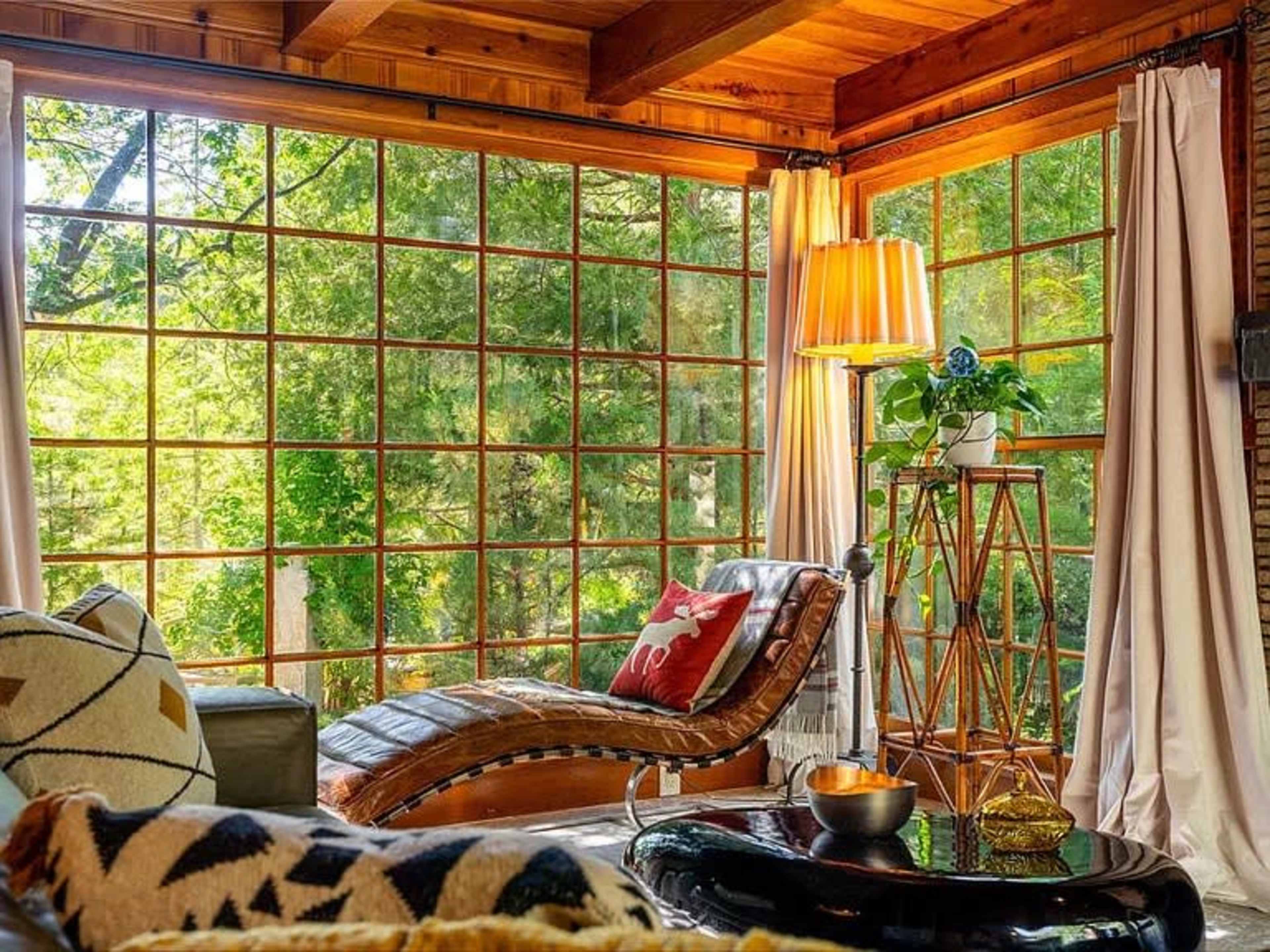 A cozy room features a large window with wooden frames, a chaise lounge, a floor lamp, and a decorative plant on a stand.