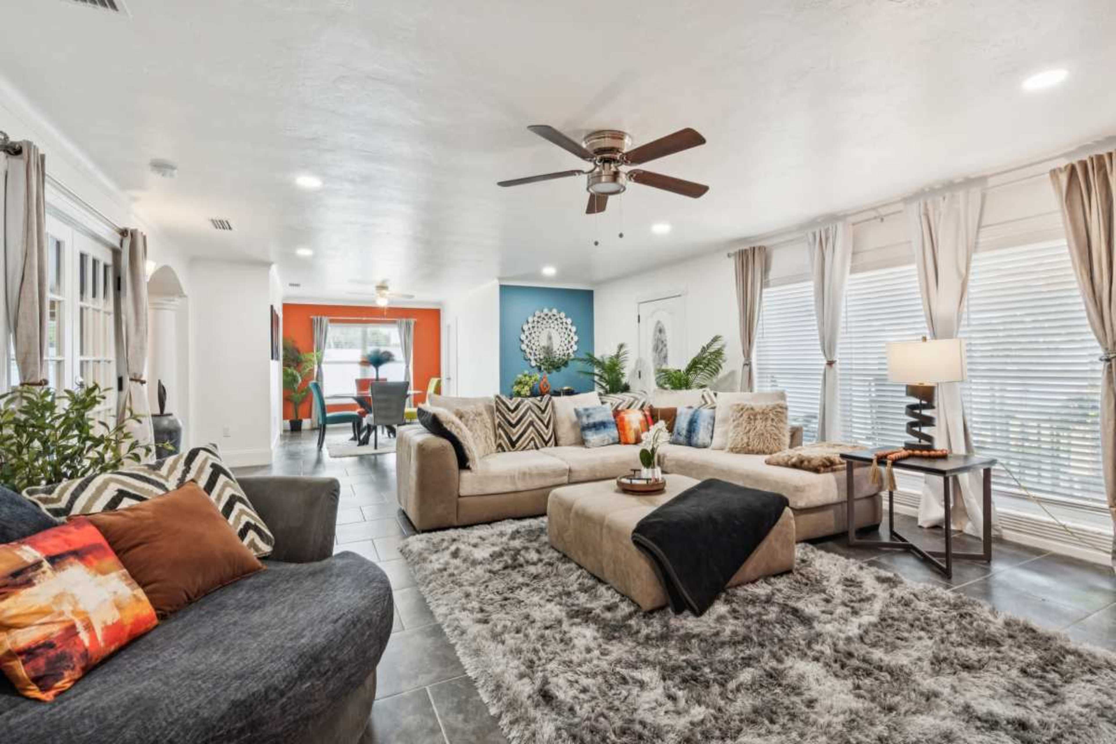 The living room features a large sectional sofa, a coffee table on a textured rug, and an open layout with dining and colorful accent walls visible in the background.