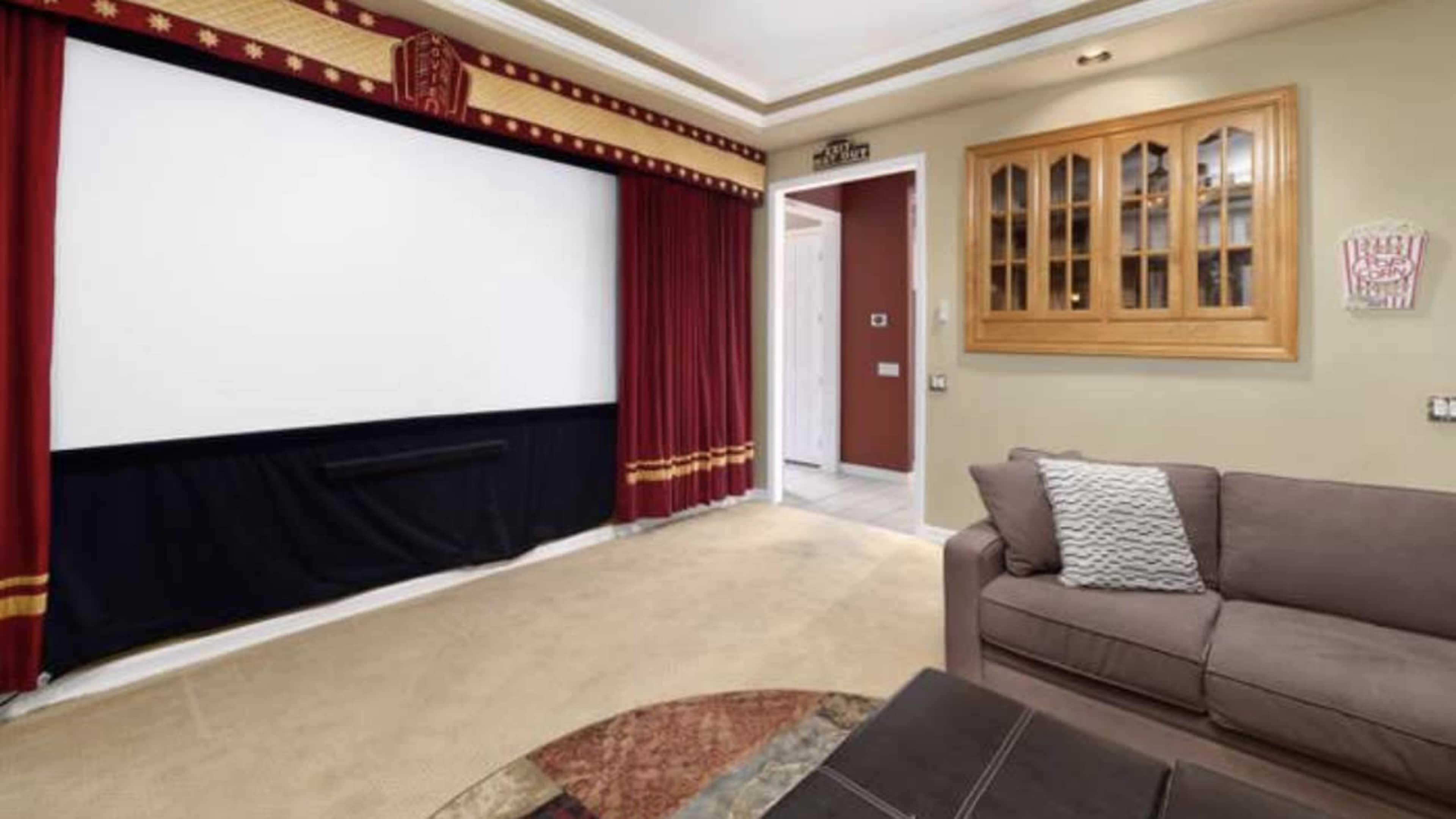 A home theater setup with a large screen framed by red curtains, a sofa, and a wall cabinet.