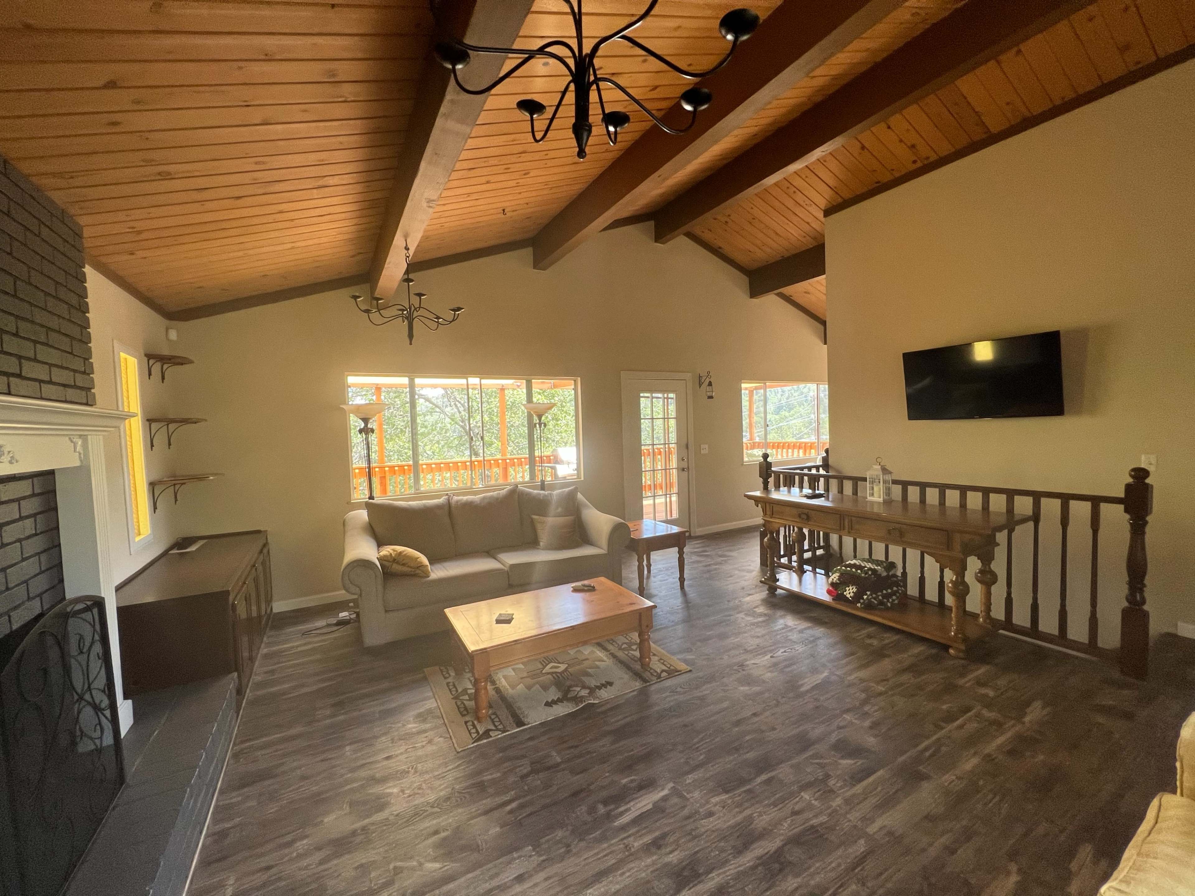 A living room with a ceiling featuring exposed wooden beams, a sofa, a coffee table, and a television mounted on the wall.