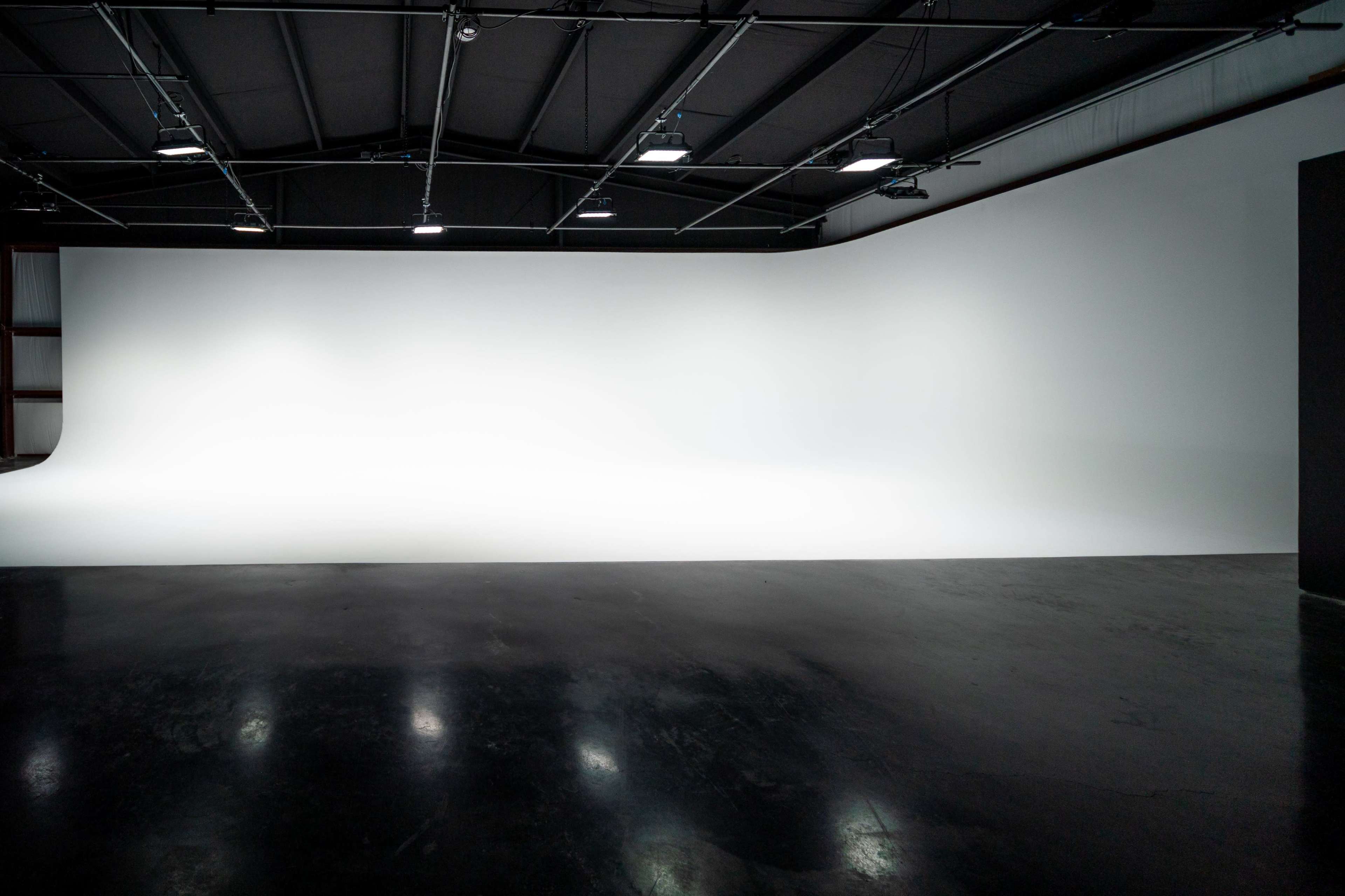 The image shows a spacious studio with a large, seamless white backdrop and polished dark flooring.