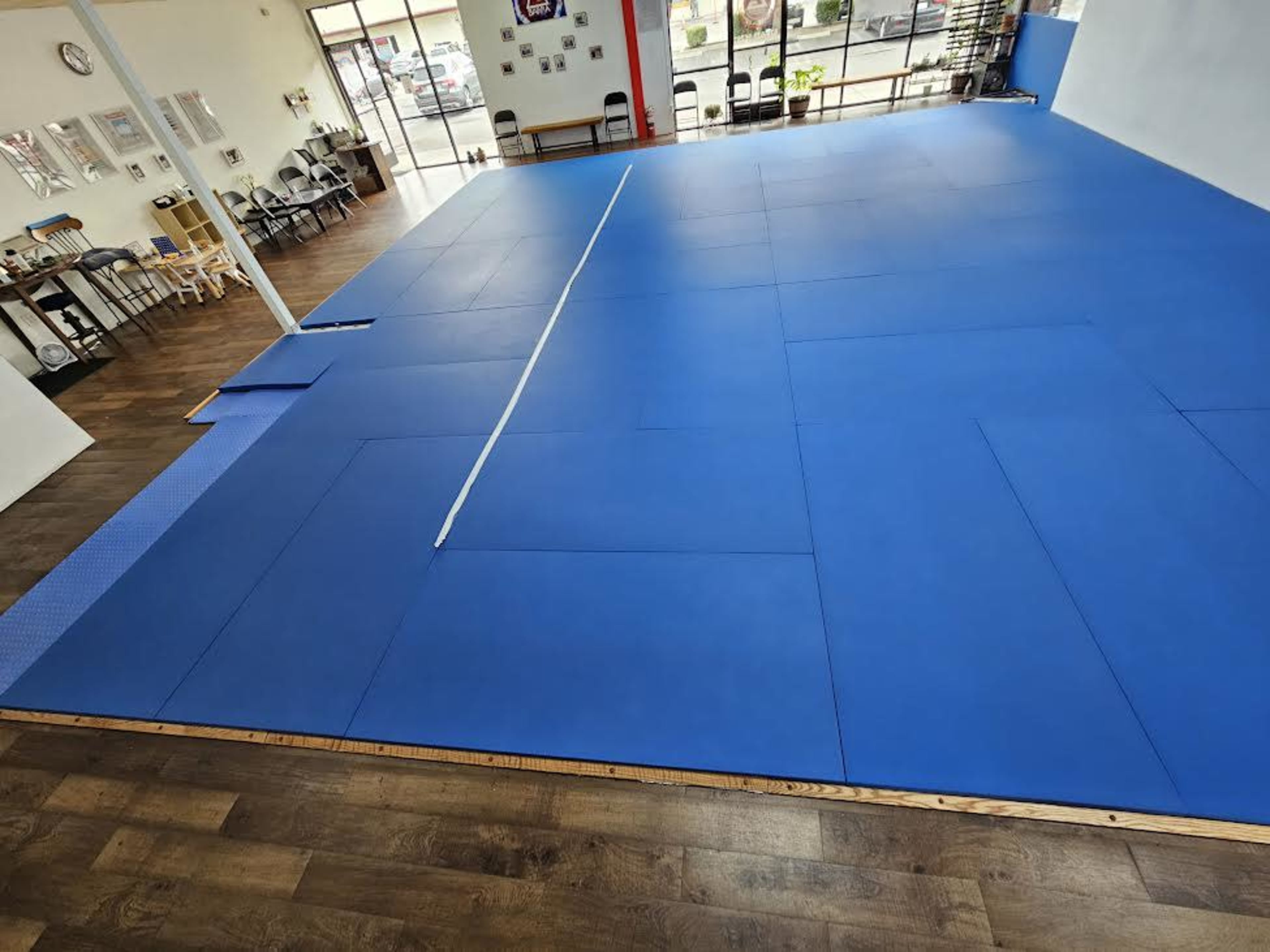 The image shows a blue mat covering a training space with wooden flooring and tables in the background.