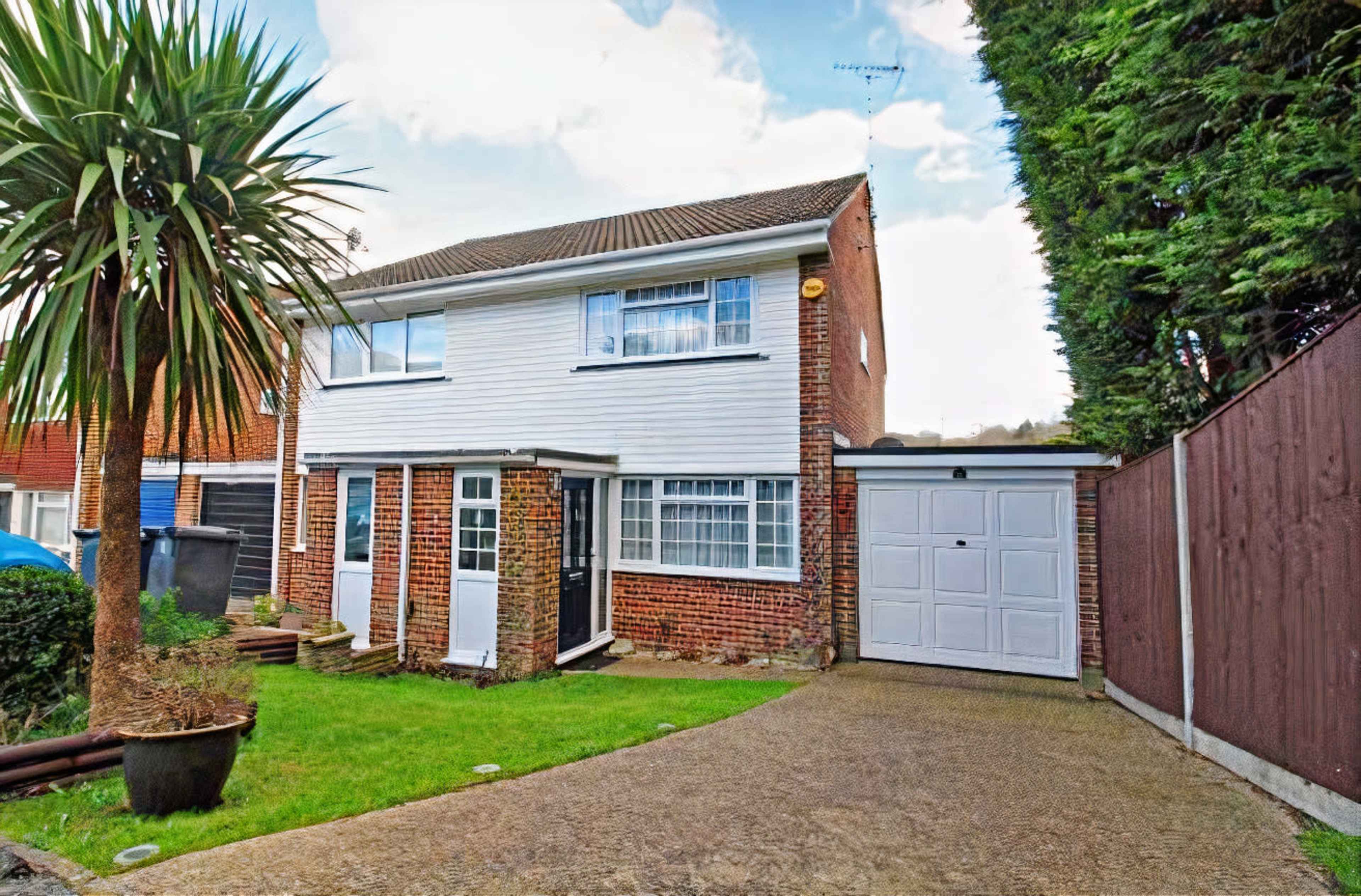 The image shows a two-story house with a brick and white exterior, a driveway, and a garage on the left side, surrounded by greenery.
