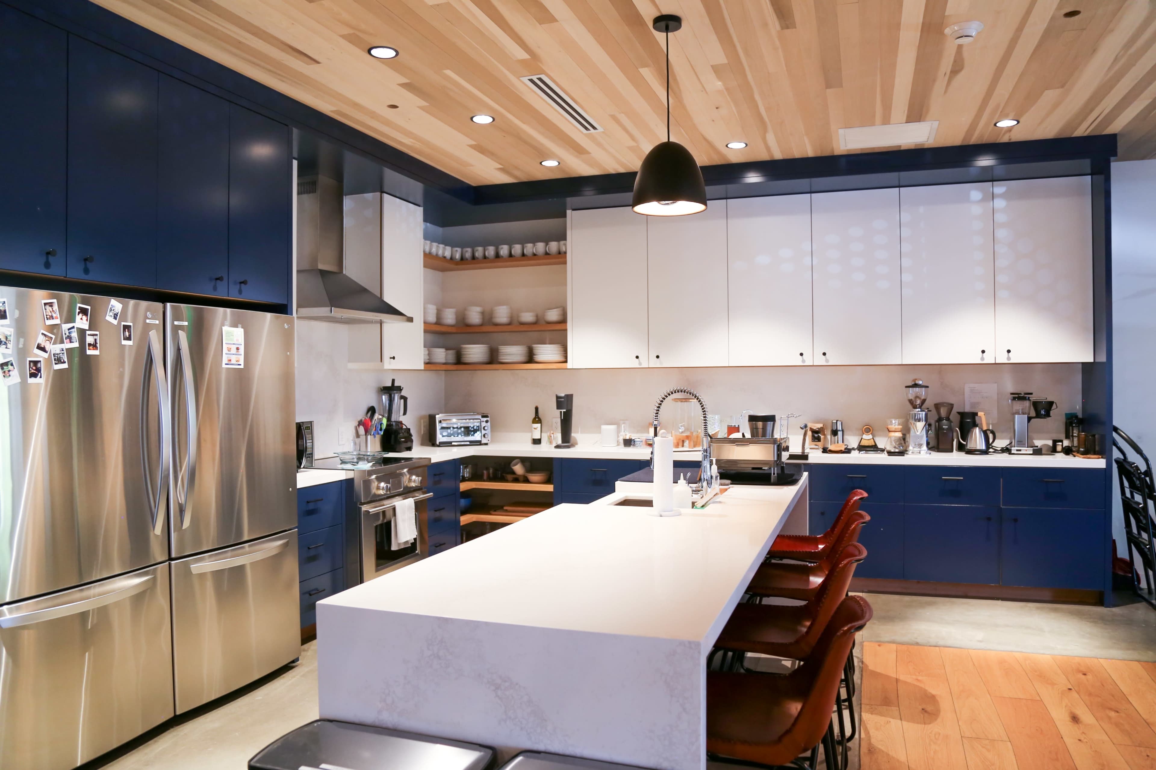 The kitchen features blue and white cabinetry, stainless steel appliances, a large countertop island, and wooden flooring.