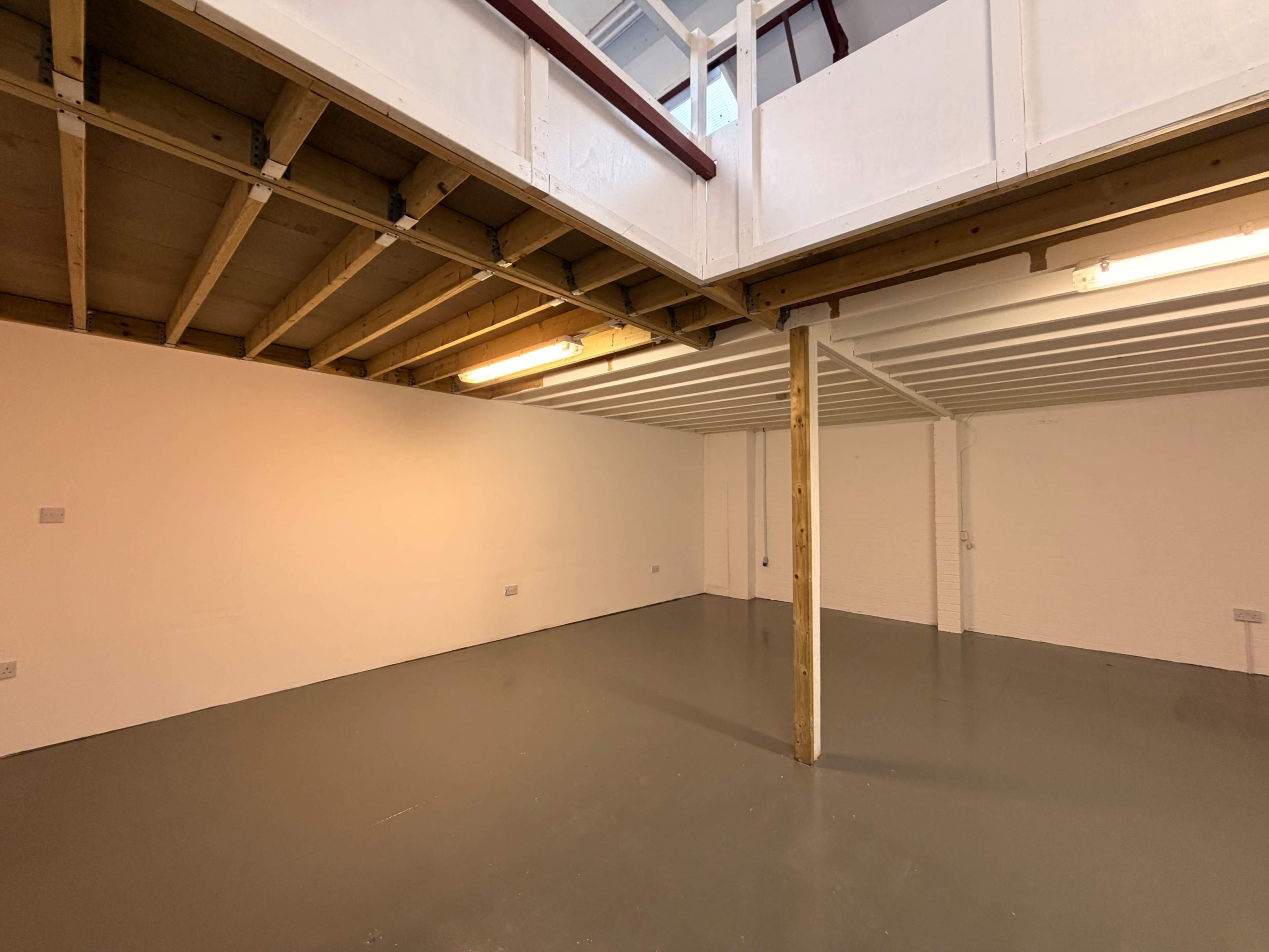 The image shows a spacious, empty basement area with a wooden support column and a mezzanine level above.