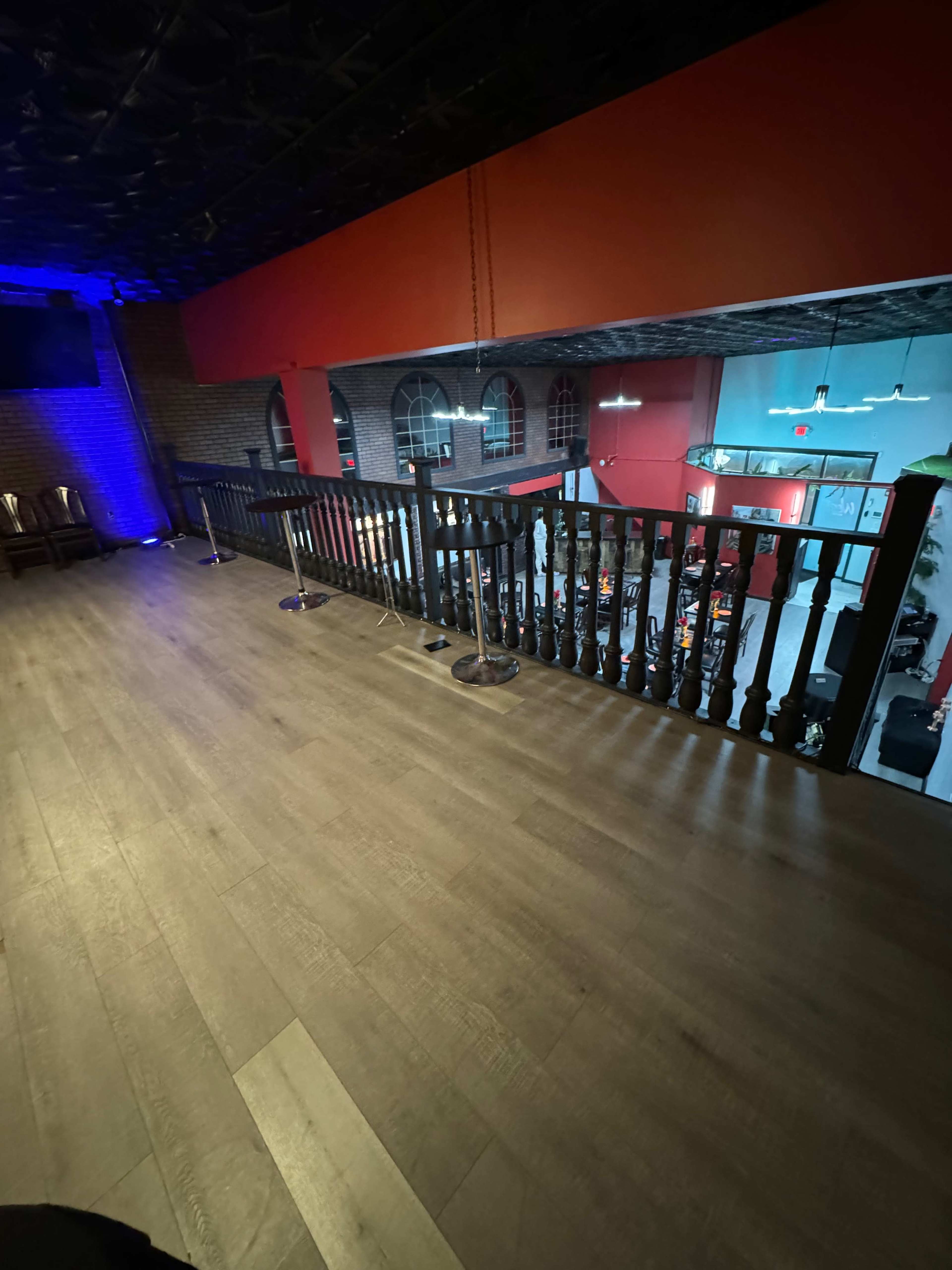 A wooden railing overlooks a dimly lit interior space with tables and red walls.