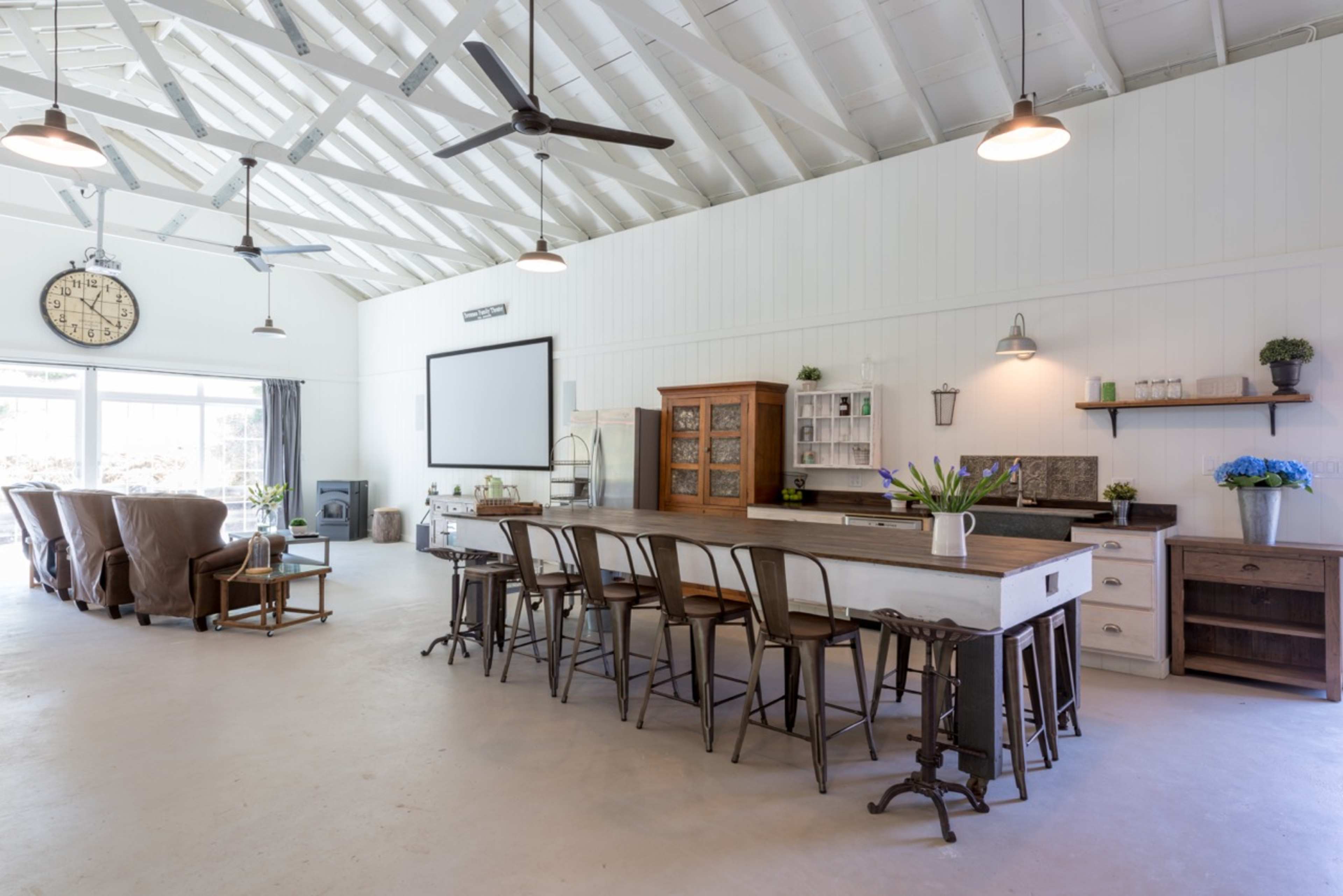 A spacious, modern kitchen and dining area with a large table, wooden furniture, and a high ceiling with exposed beams.