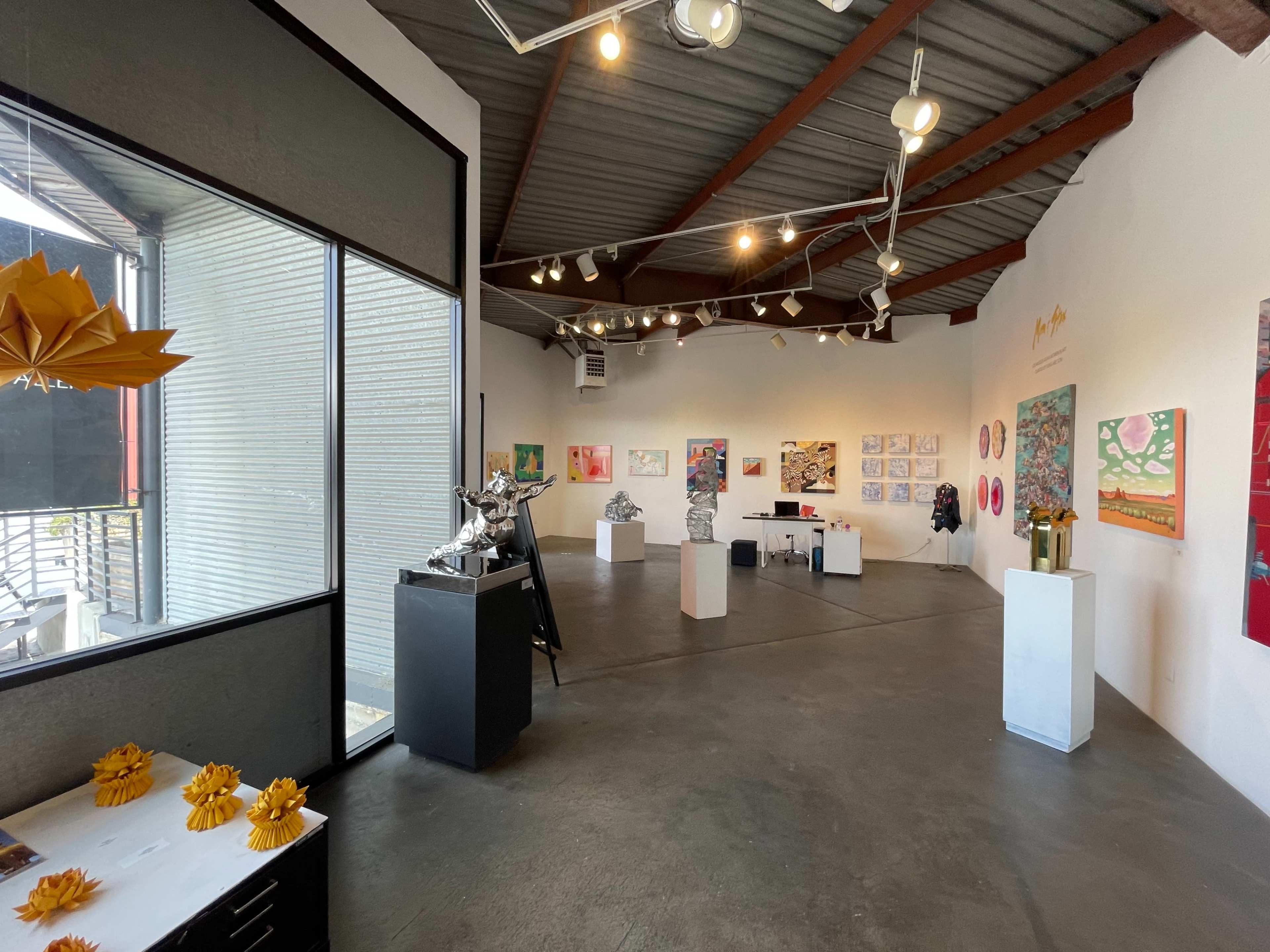 An art gallery interior with various artworks displayed on the walls and sculptures on pedestals throughout the space.