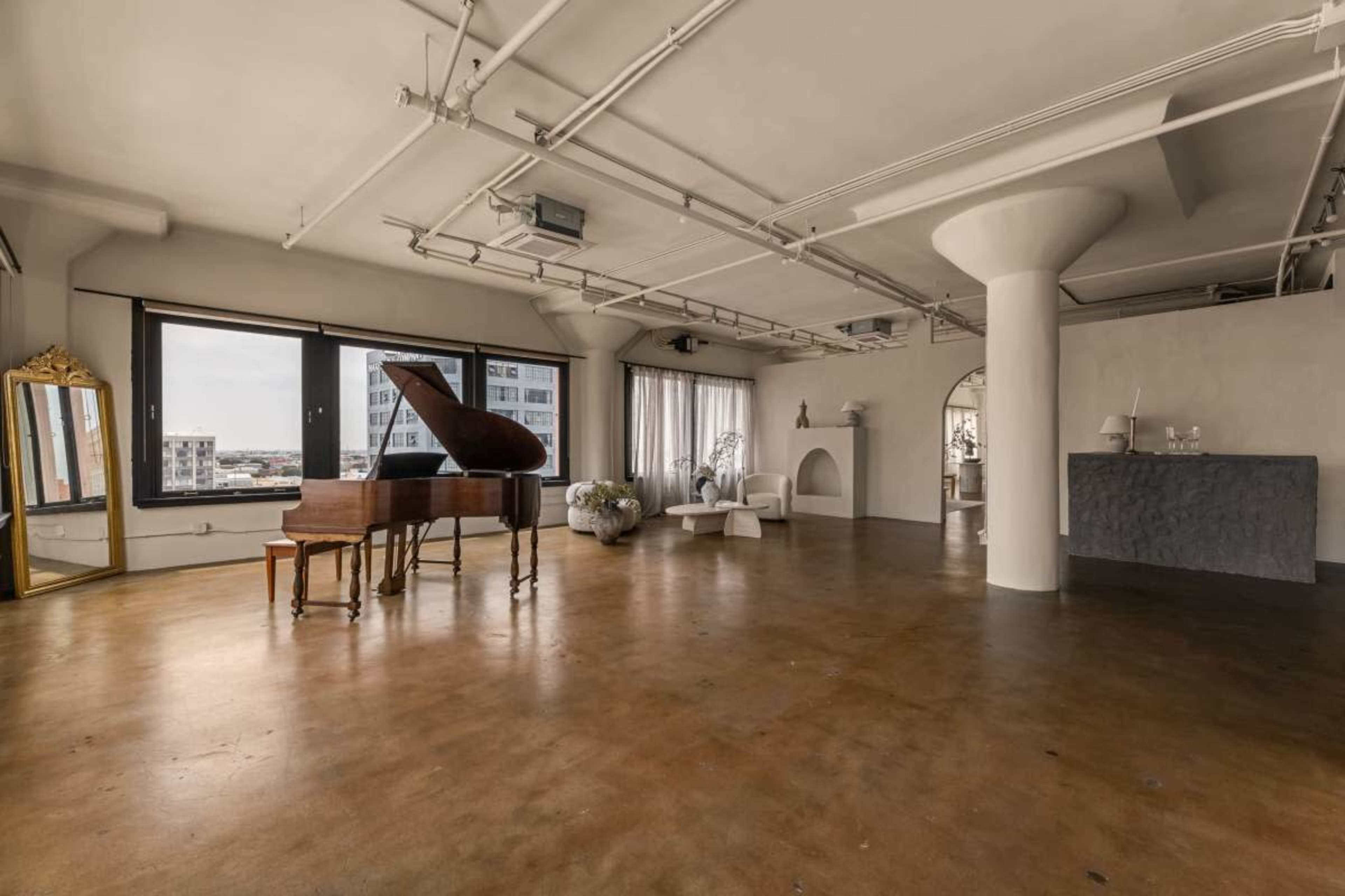 A spacious, minimalistic interior features a grand piano, modern furniture, and large windows offering city views.