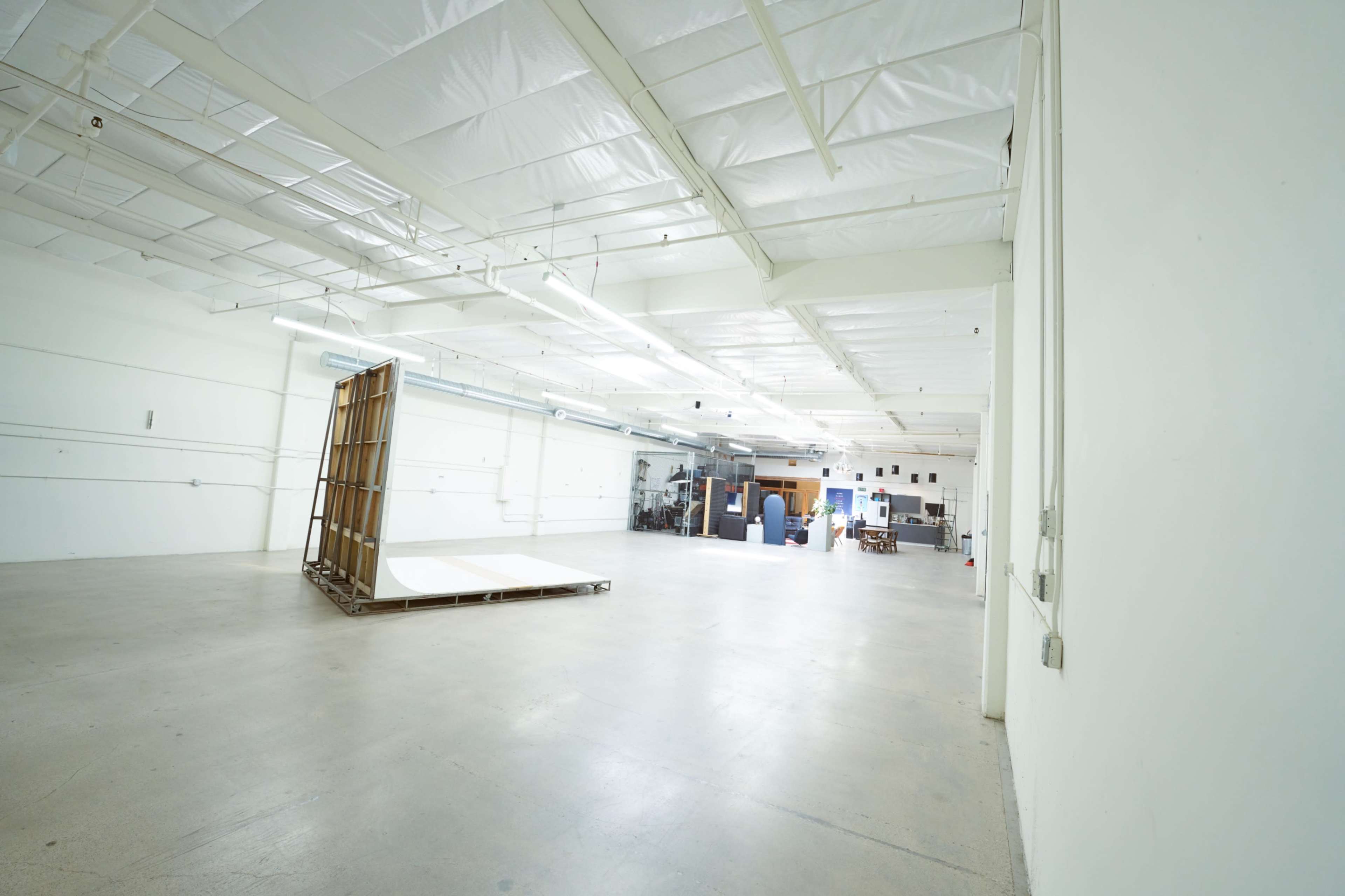 The image shows a spacious, empty warehouse with high ceilings and a large wooden structure in the foreground.
