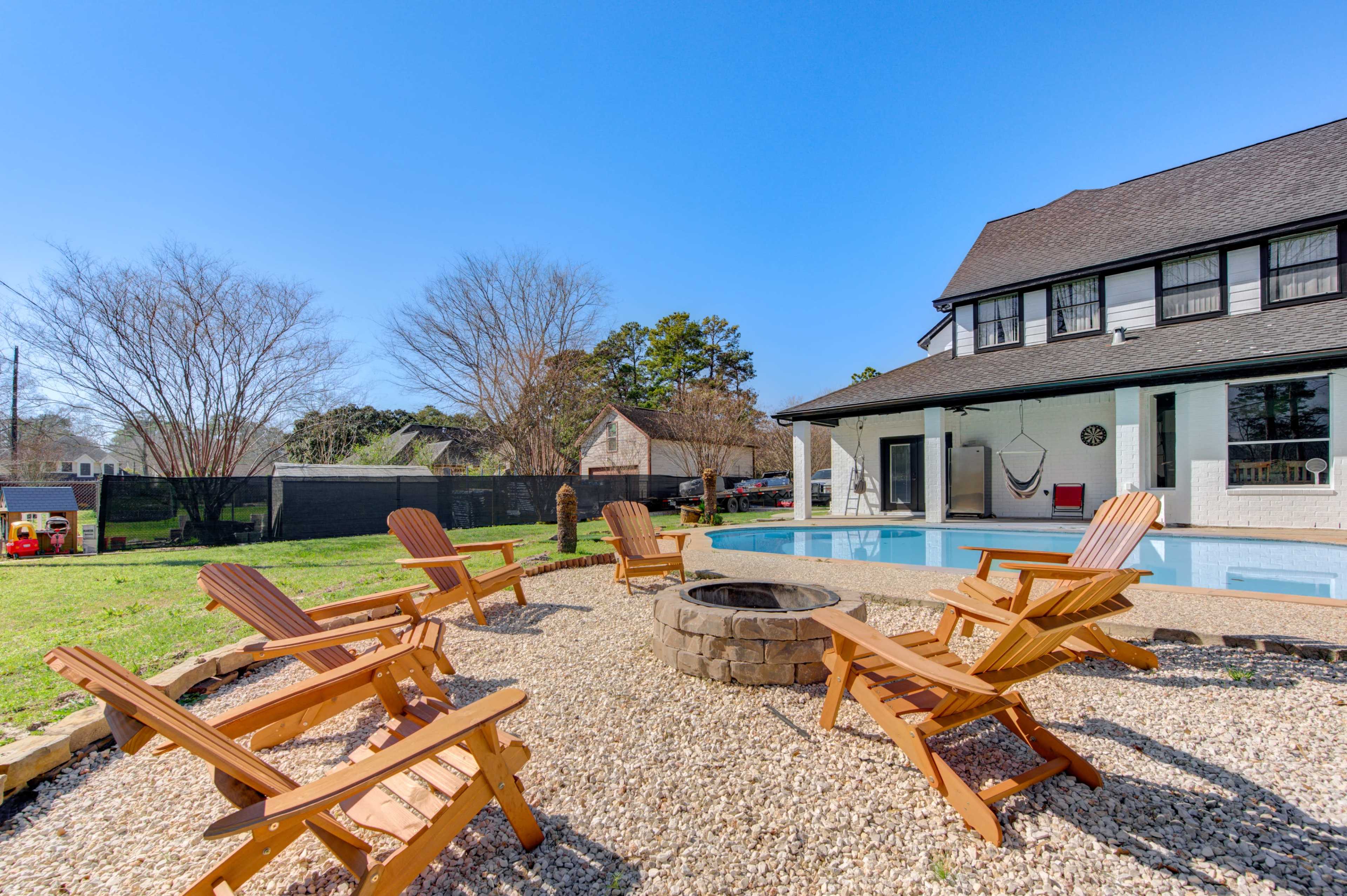 The scene shows a backyard with a swimming pool, surrounded by wooden lounge chairs and a fire pit, with a house and trees in the background.