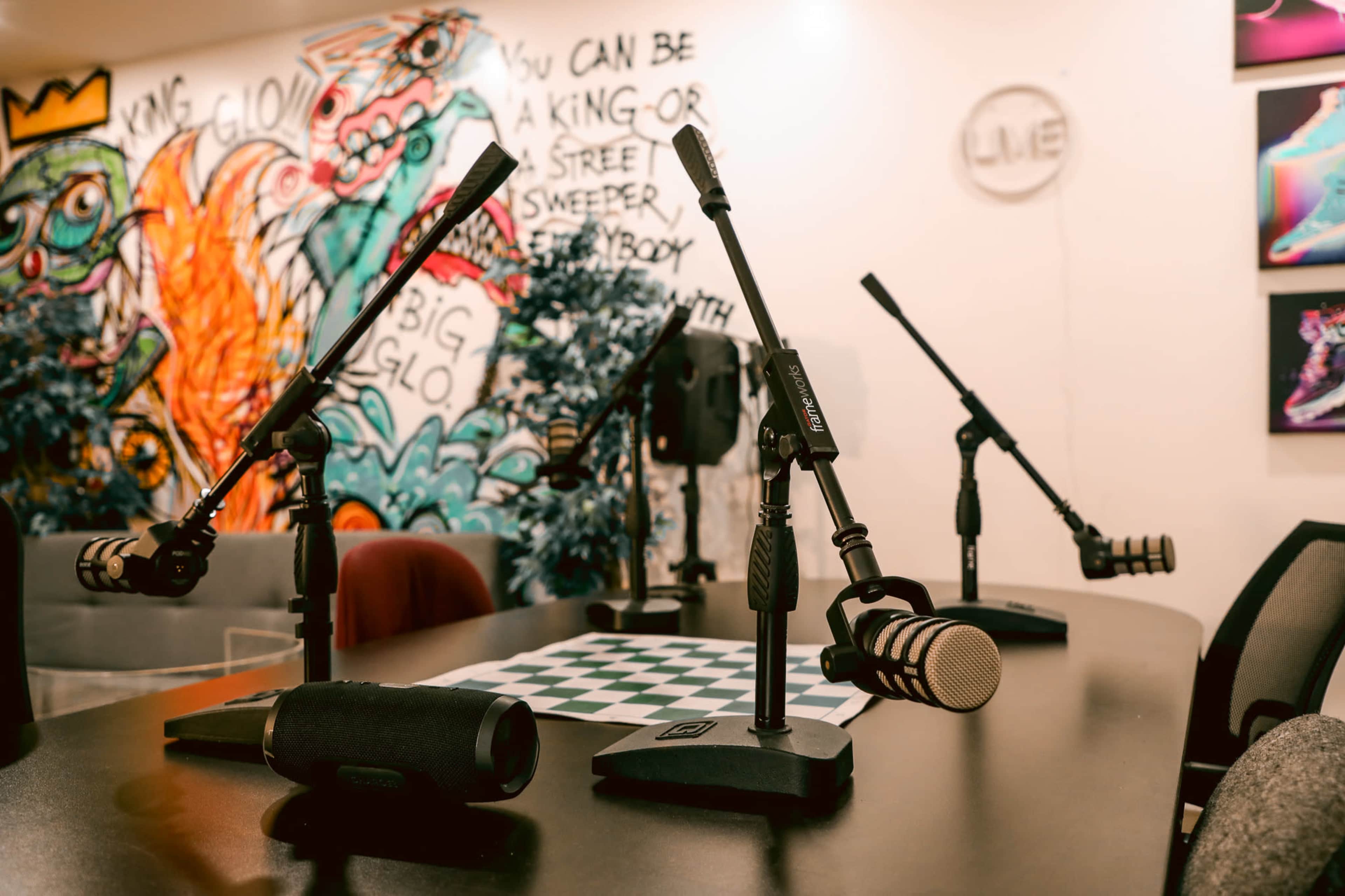 A recording studio set up with multiple microphones and a checkered table in front of a colorful mural on the wall.