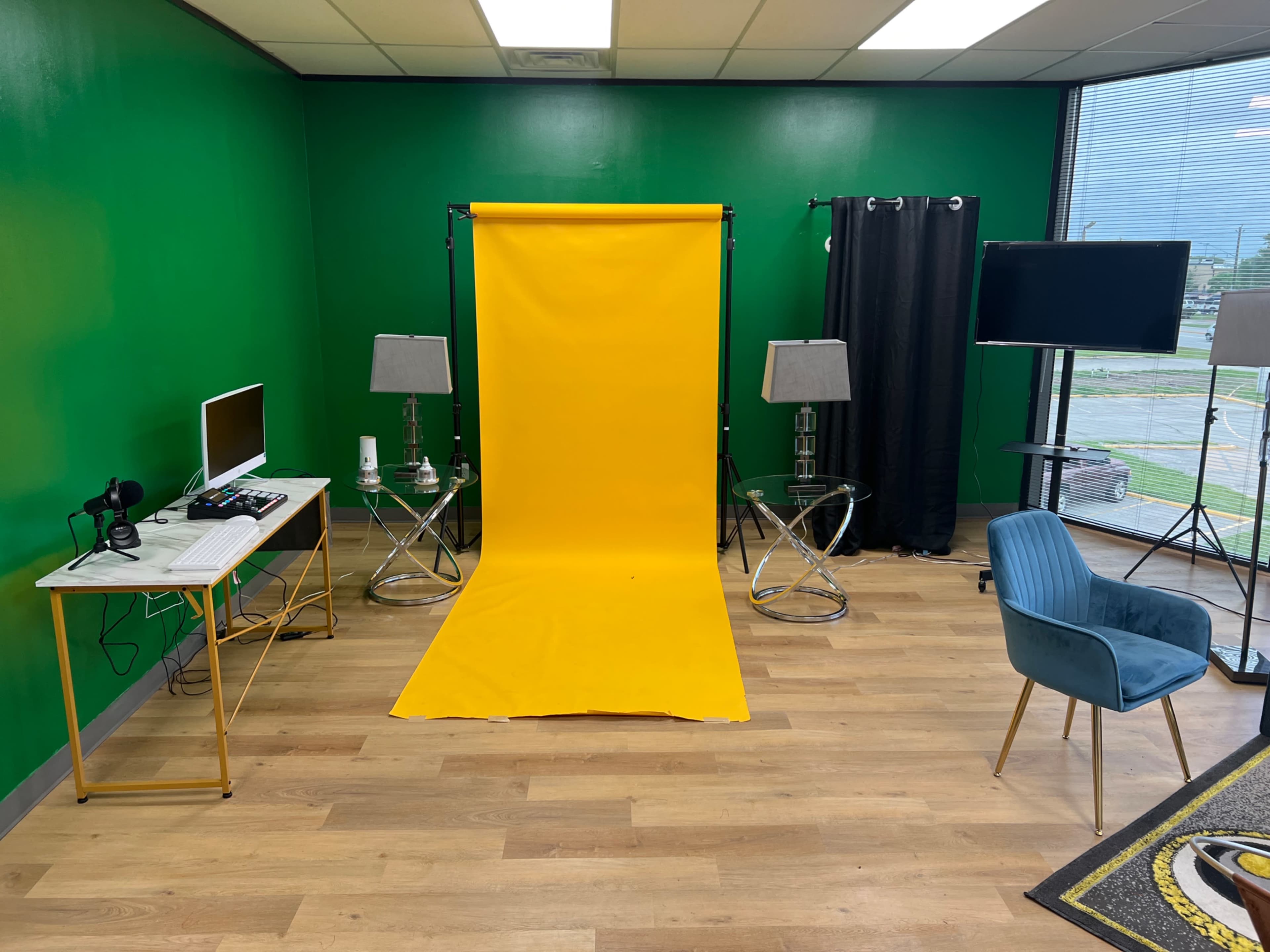 A studio space with a bright green wall, a yellow backdrop, two lamps, a computer station, and a blue chair.