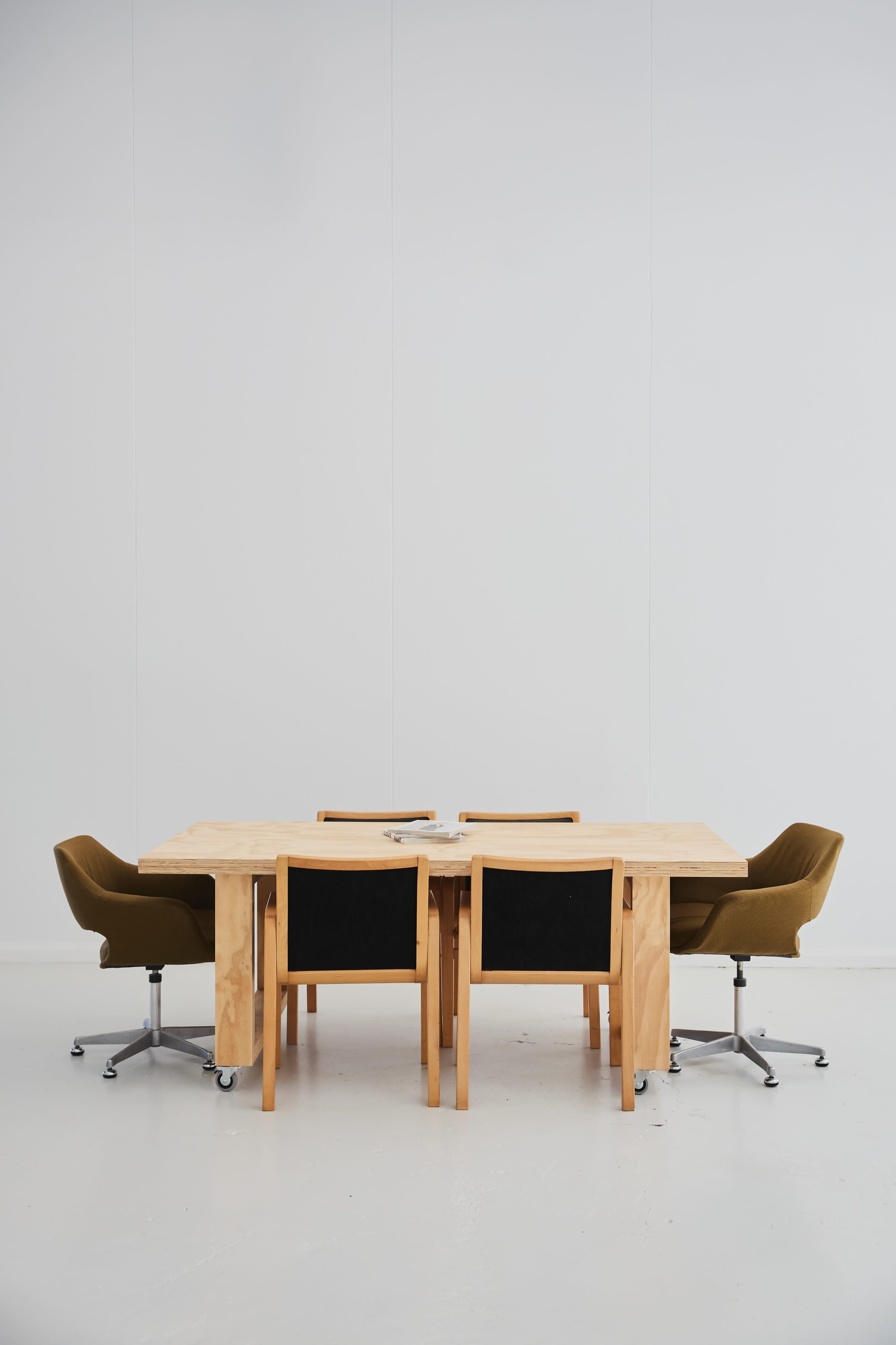 The image shows a wooden table surrounded by four chairs in a minimalistic, light-colored room.