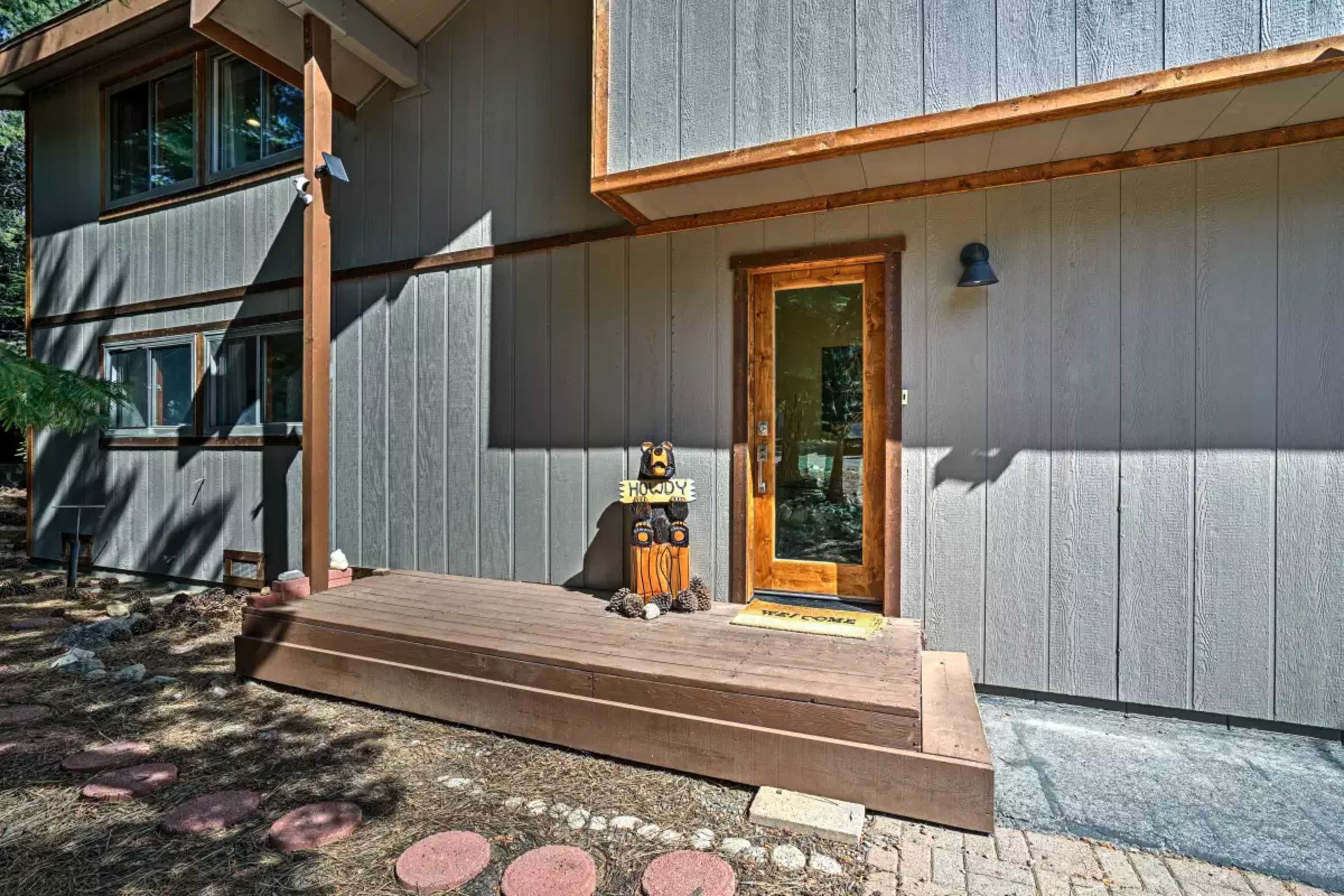 A welcoming entrance with a wooden deck and a sign next to the front door of a house that features gray siding.