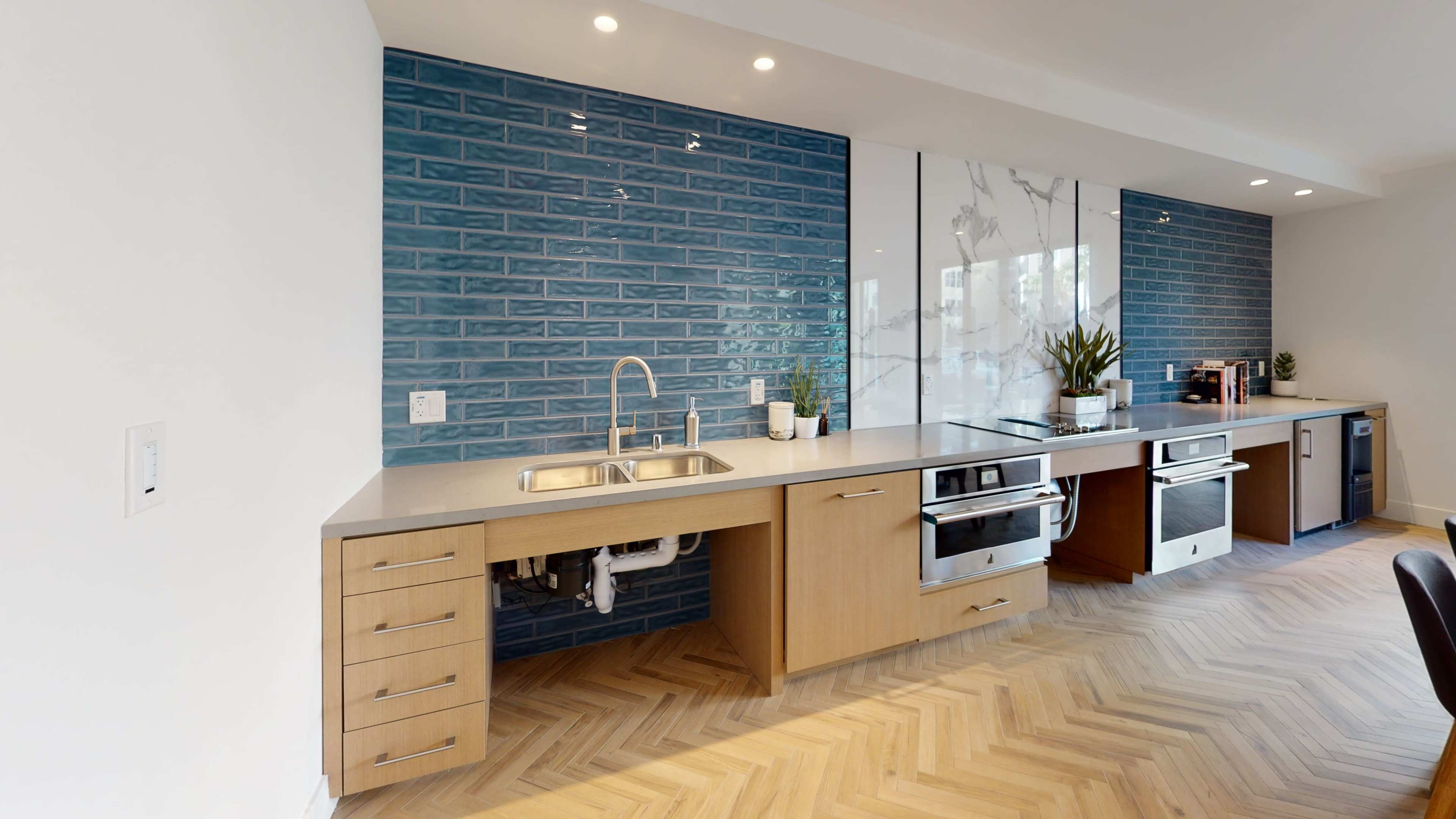 A modern kitchen with blue tiled walls, a stainless steel sink, and a herringbone pattern wooden floor.