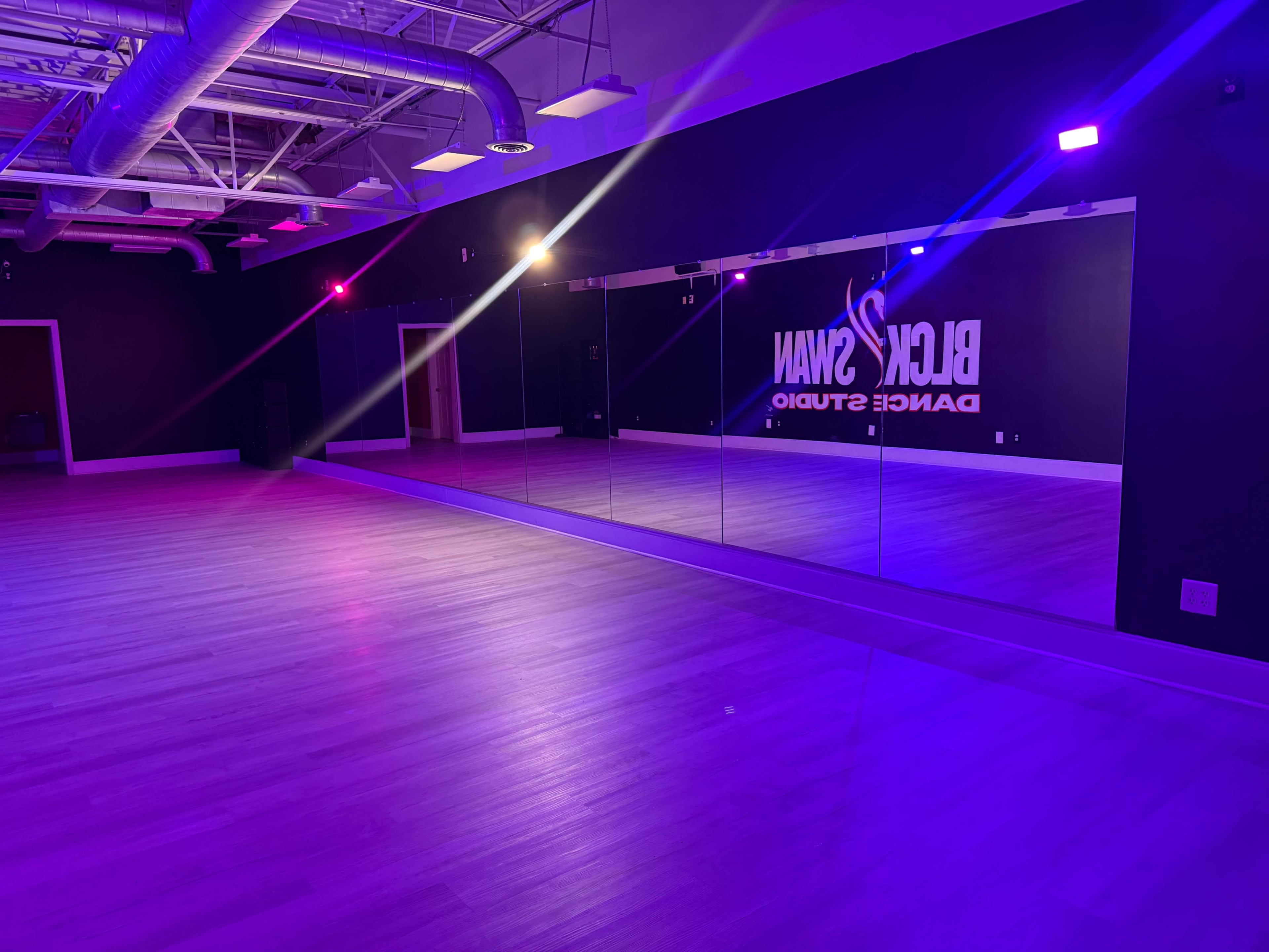 The image shows a dance studio with purple and pink lighting and a mirrored wall featuring the name "Black Swan Dance Studio."