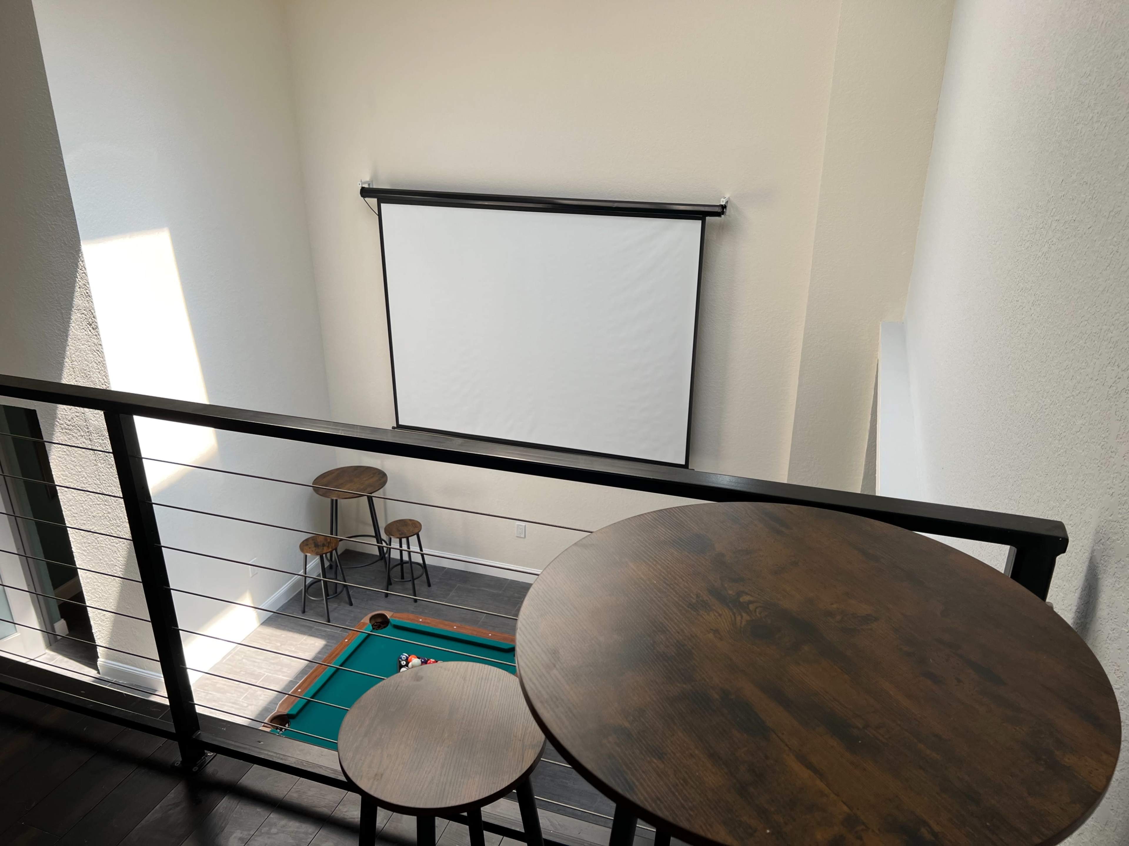 A second-floor view of a leisure area featuring a pool table, a projection screen, and two small round tables.