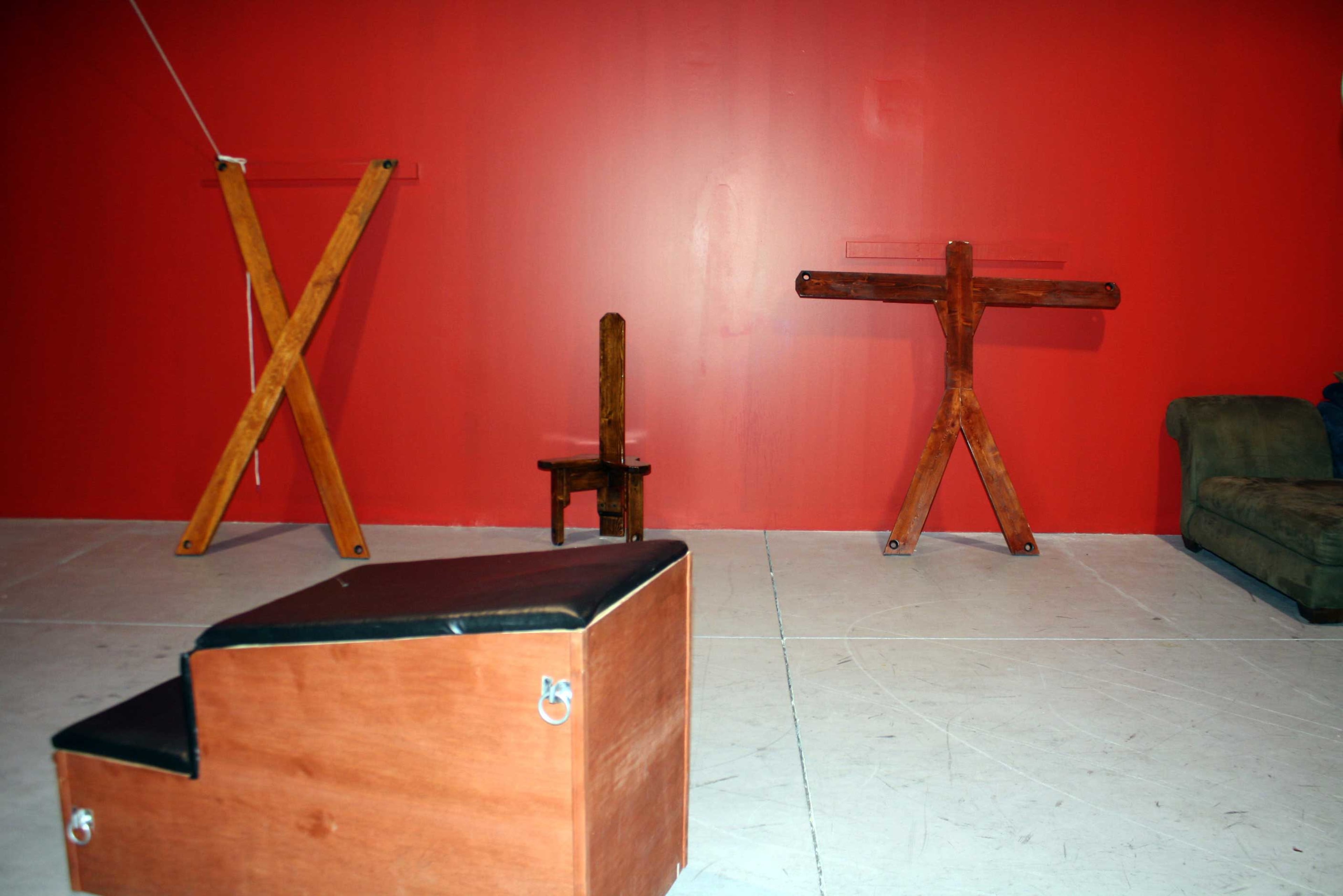 A red wall with wooden frames and a chair positioned on a white floor, alongside a brown couch.