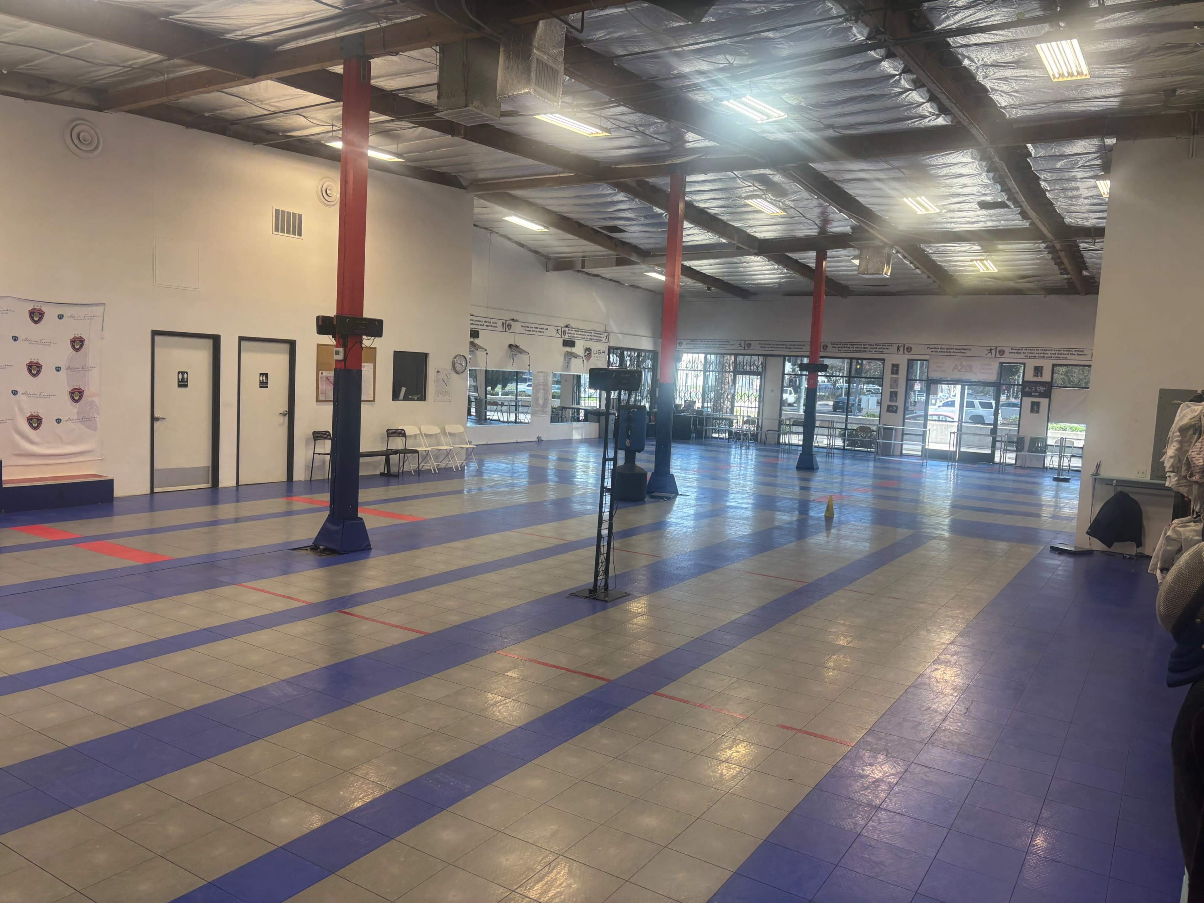 The image shows an empty indoor sports facility with a polished floor marked for games and several basketball hoops.
