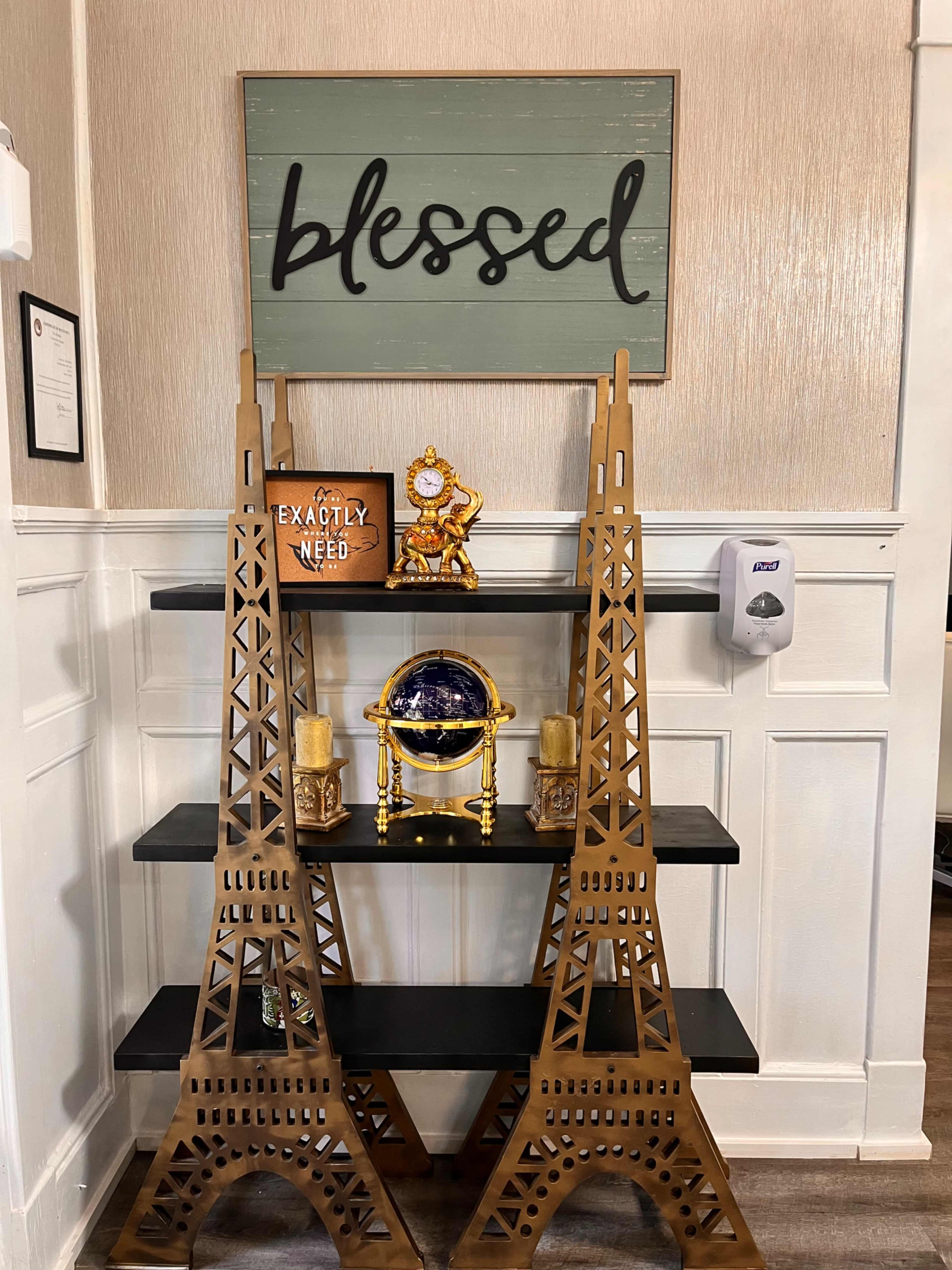 A wooden shelf with two Eiffel Tower decorative pieces on either side, displaying a globe and candles, beneath a sign that reads "blessed."