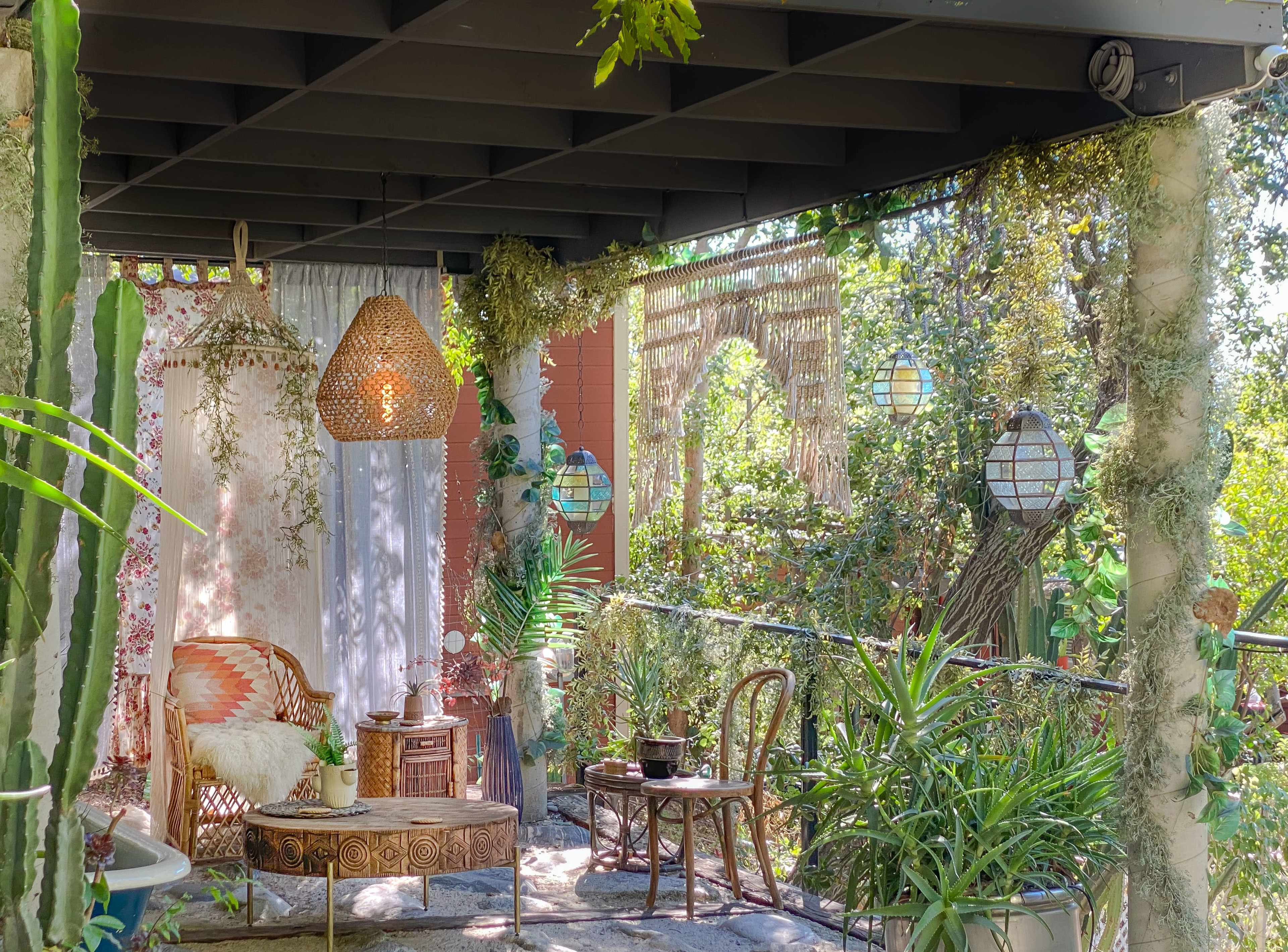 A cozy outdoor patio furnished with a wicker chair, a small table, and adorned with plants and decorative hanging lanterns.
