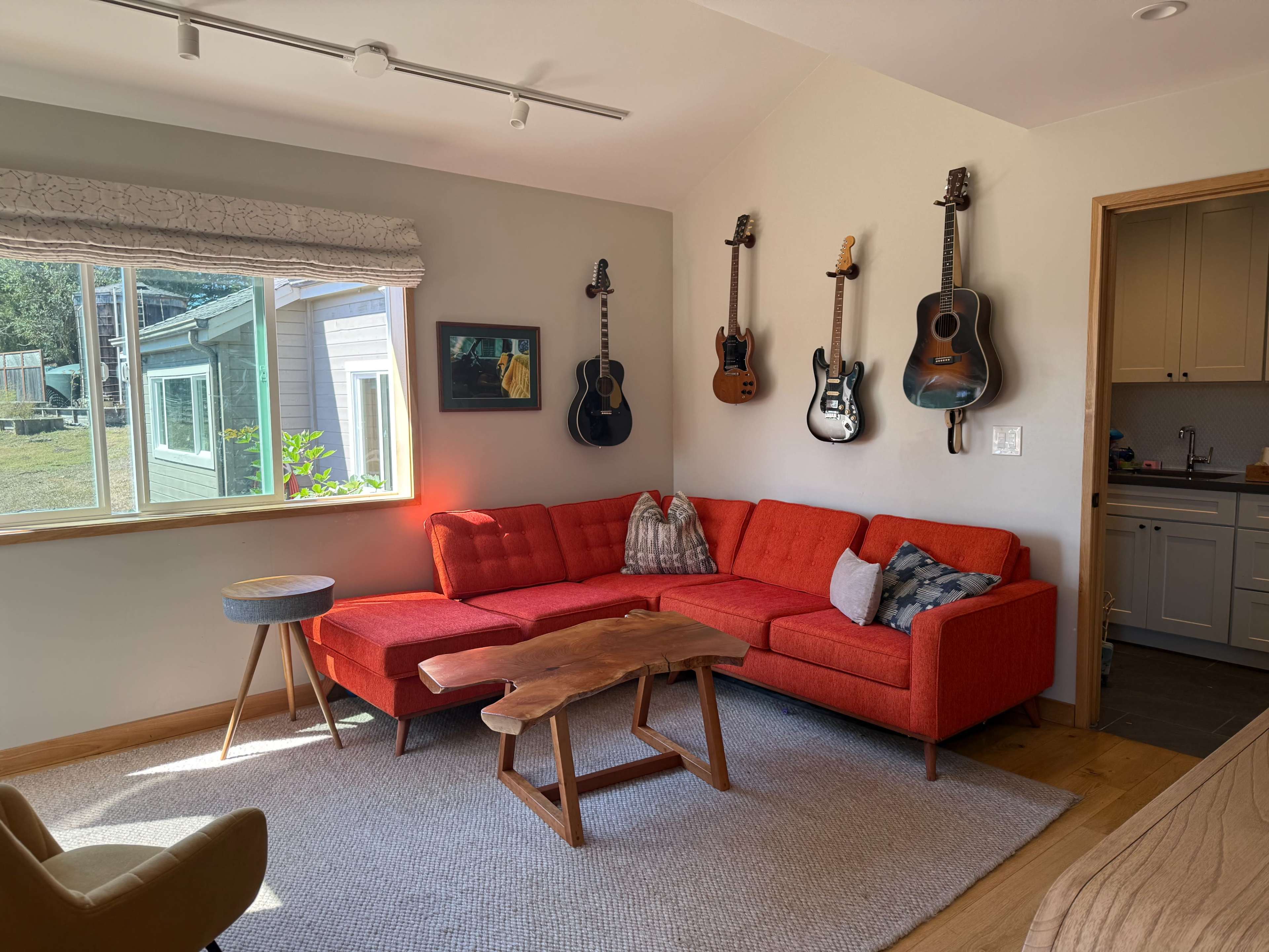 The image shows a cozy living room featuring a red sectional sofa, a wooden coffee table, and various guitars hanging on the wall.