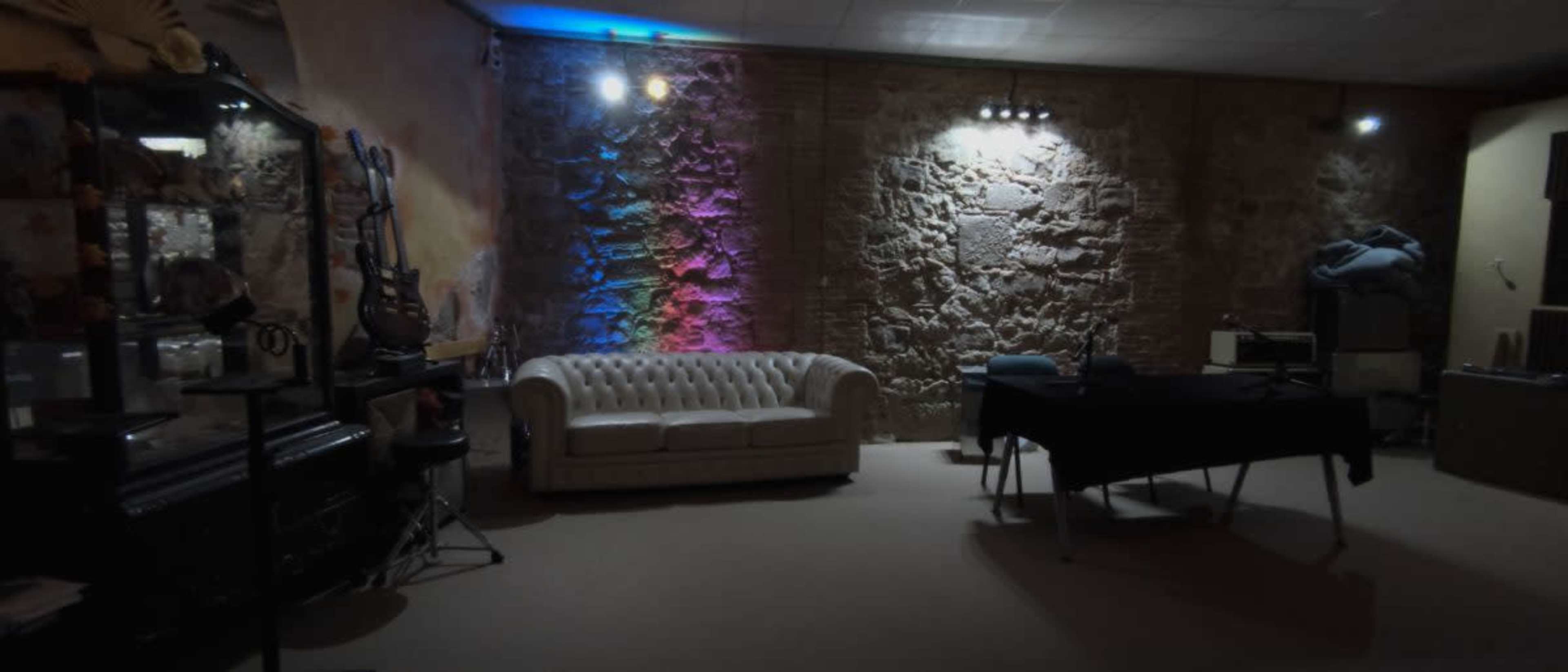 A dimly lit room with a white leather couch, a black table, and exposed stone walls illuminated by colorful lights.
