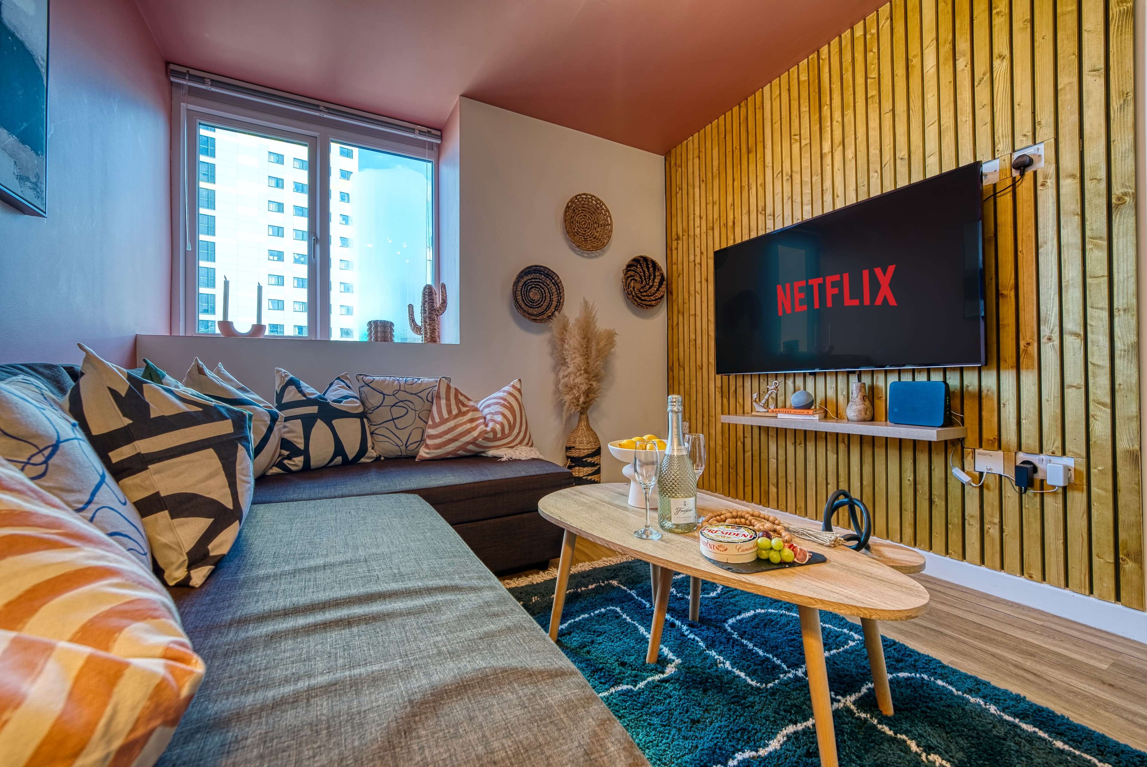 A cozy living room features a sectional sofa, a coffee table with snacks, and a large screen displaying the Netflix logo against a backdrop of wooden paneling.