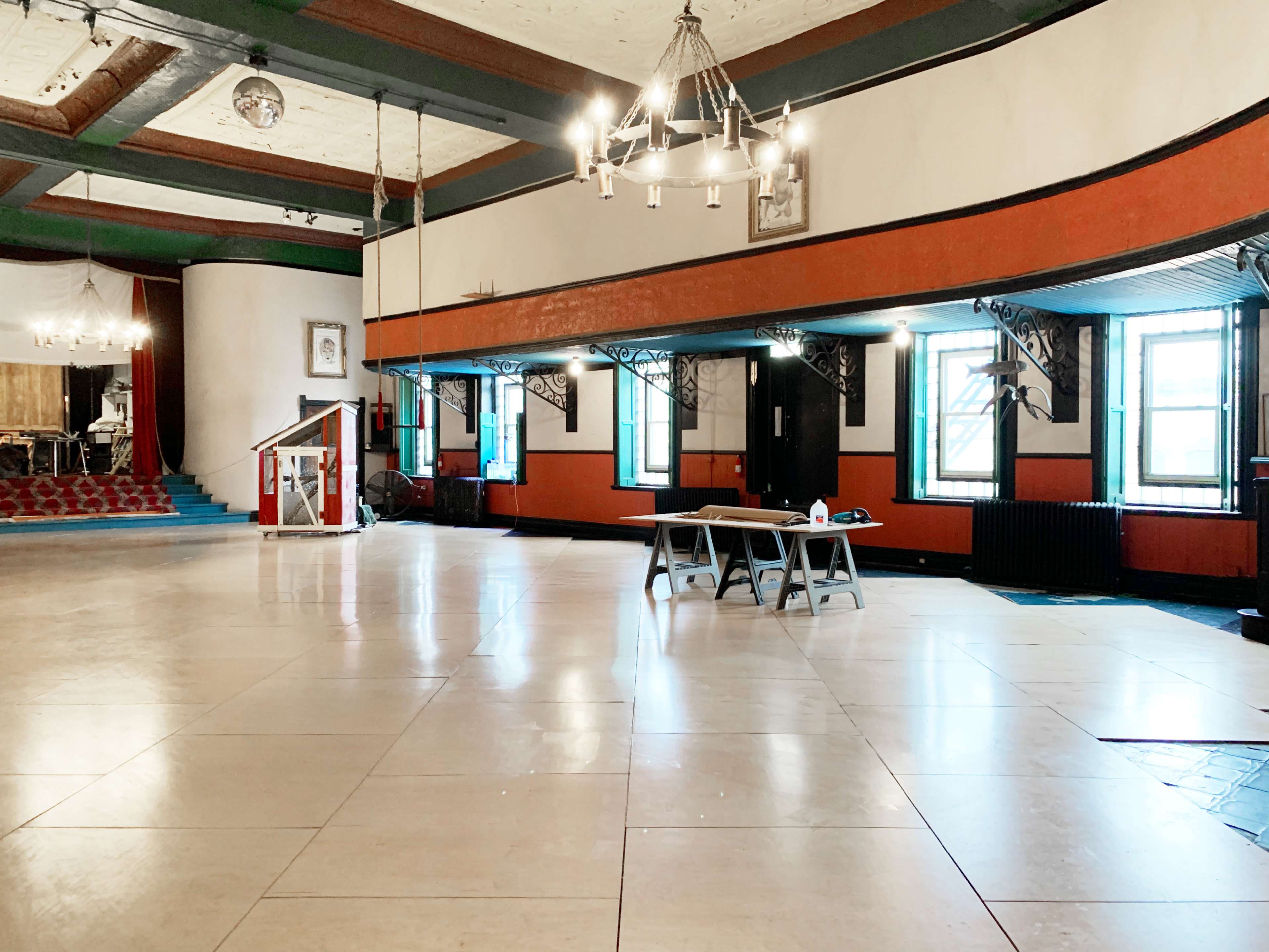 A spacious, empty room with a polished floor, large windows, and a raised platform at one end.