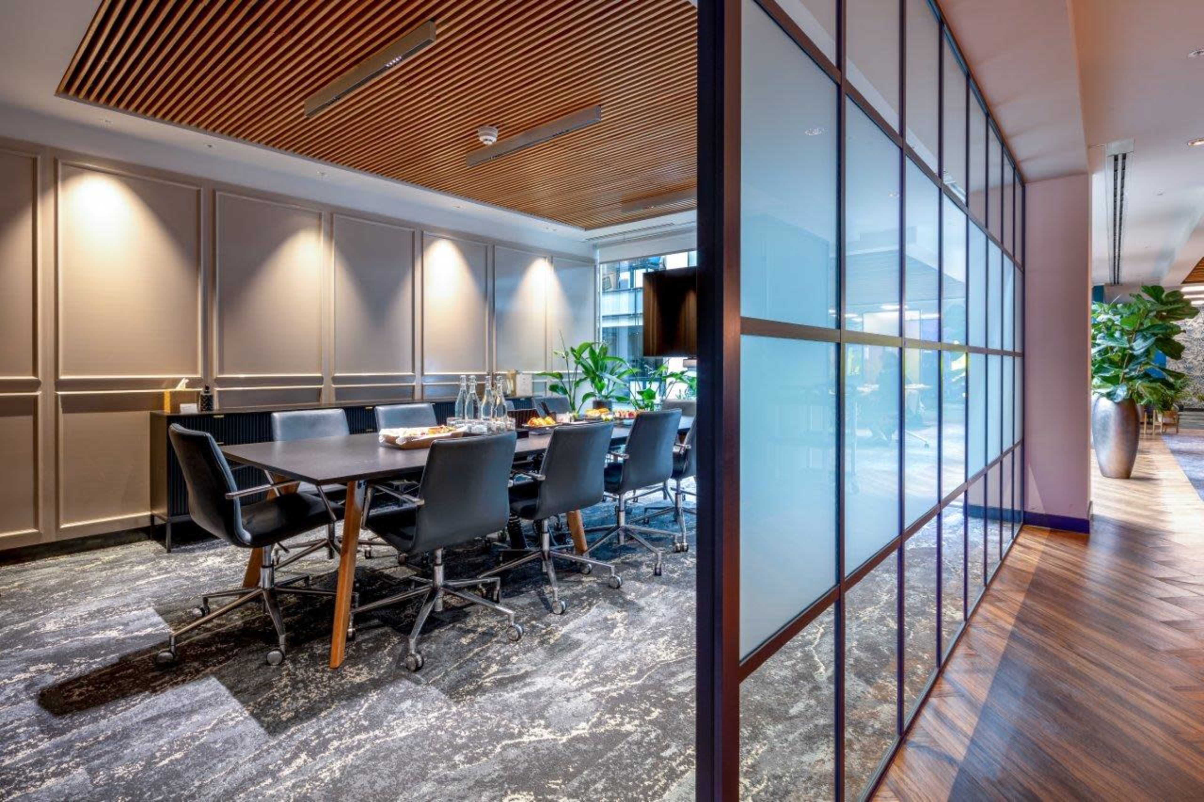 A modern conference room with a long table, black chairs, and large windows allowing natural light.