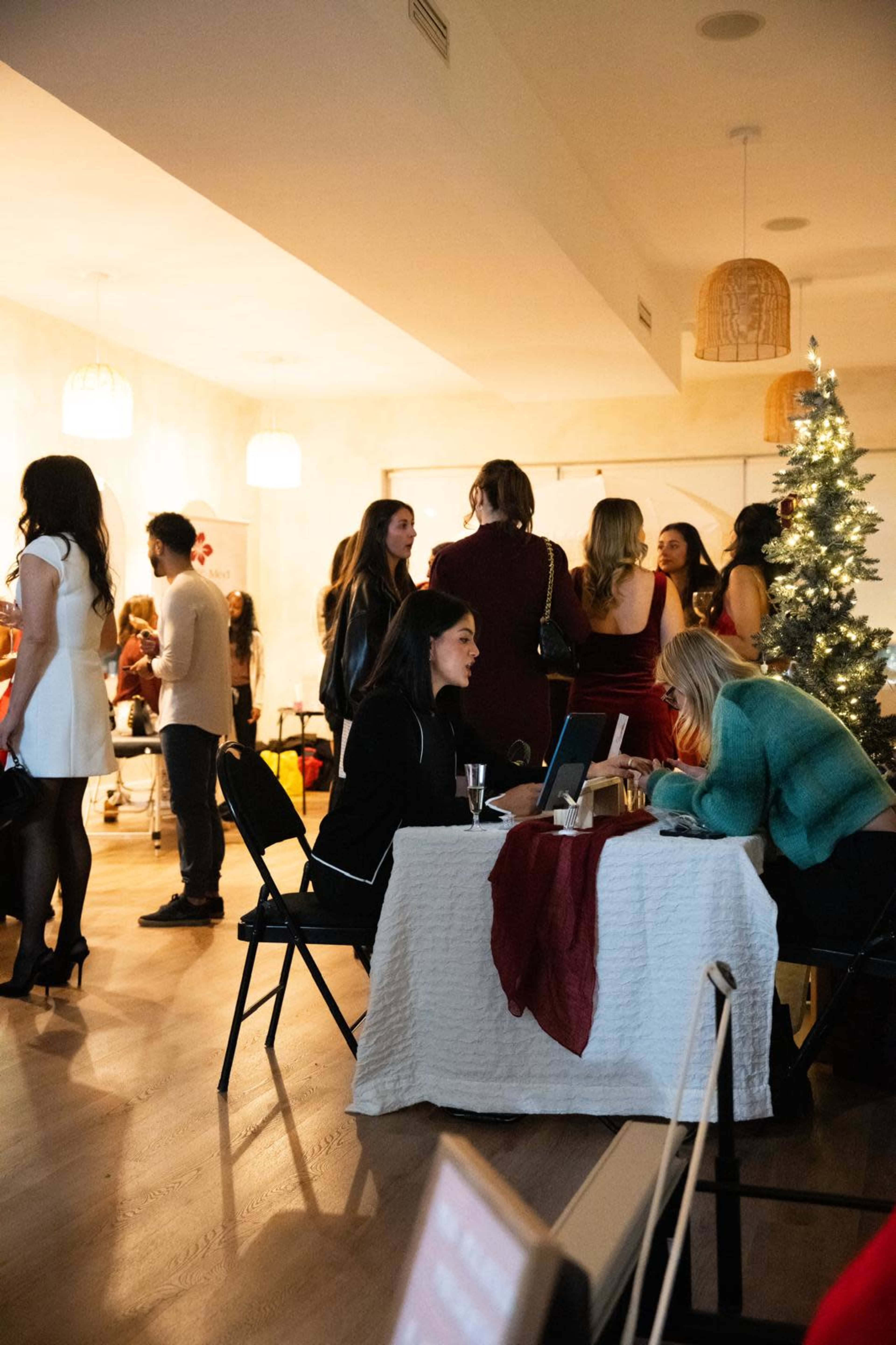 A group of people socializes in a well-decorated indoor space, featuring a Christmas tree and various festive decorations.