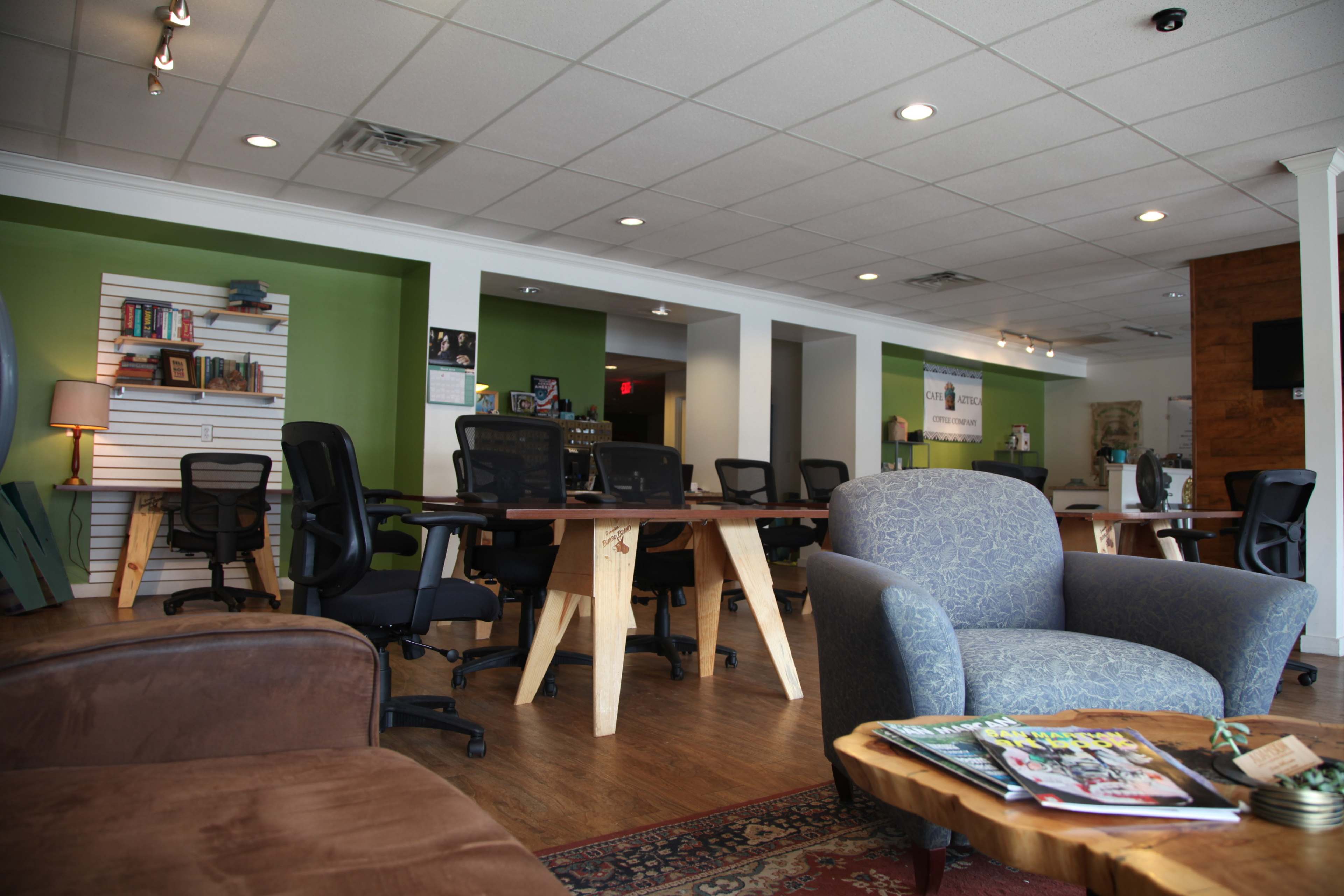 A modern office space with several desks and chairs, a cozy seating area, and green accent walls.