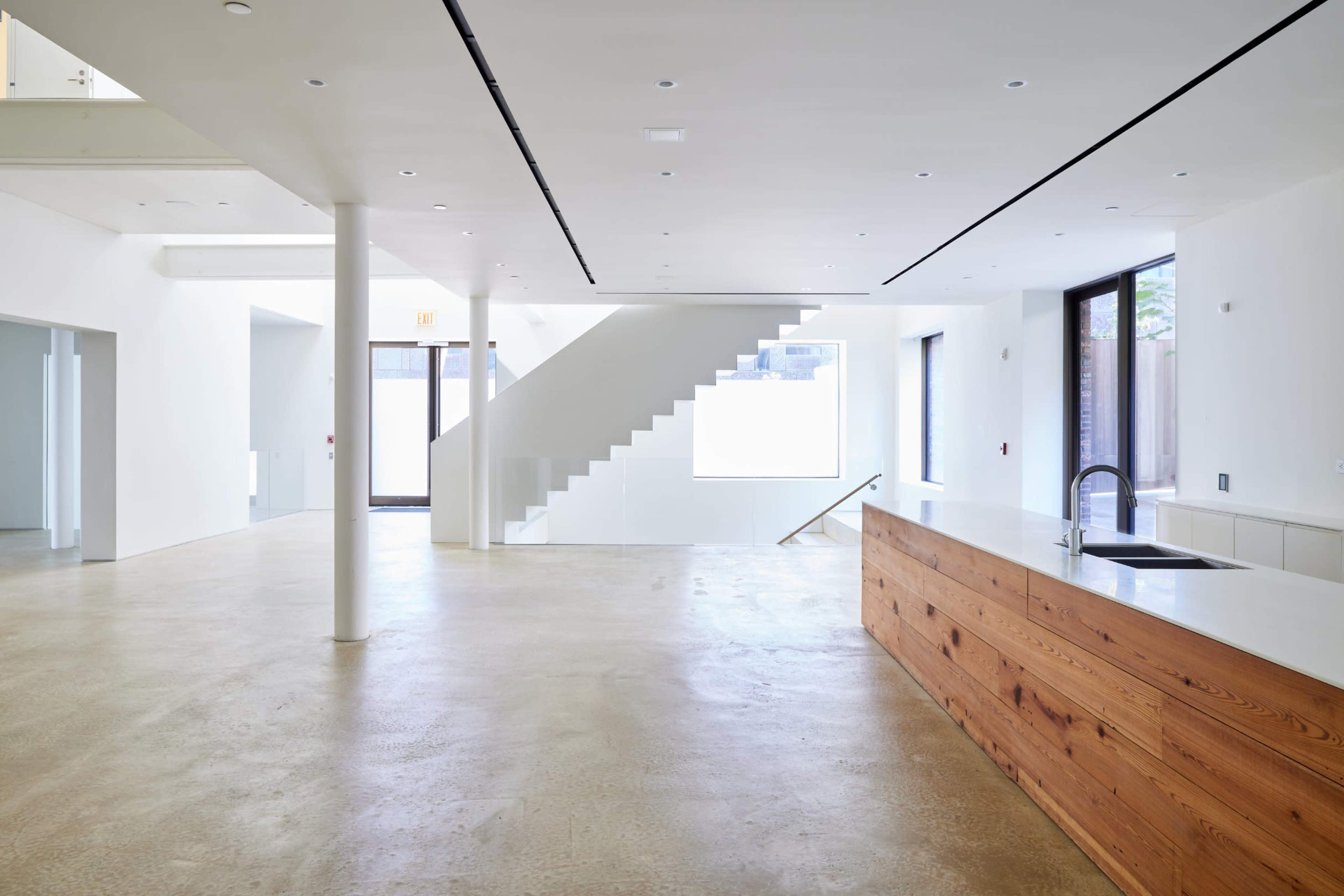 A spacious, modern interior features a large kitchen island with a wooden countertop, polished concrete floors, and stairs leading to an upper level.