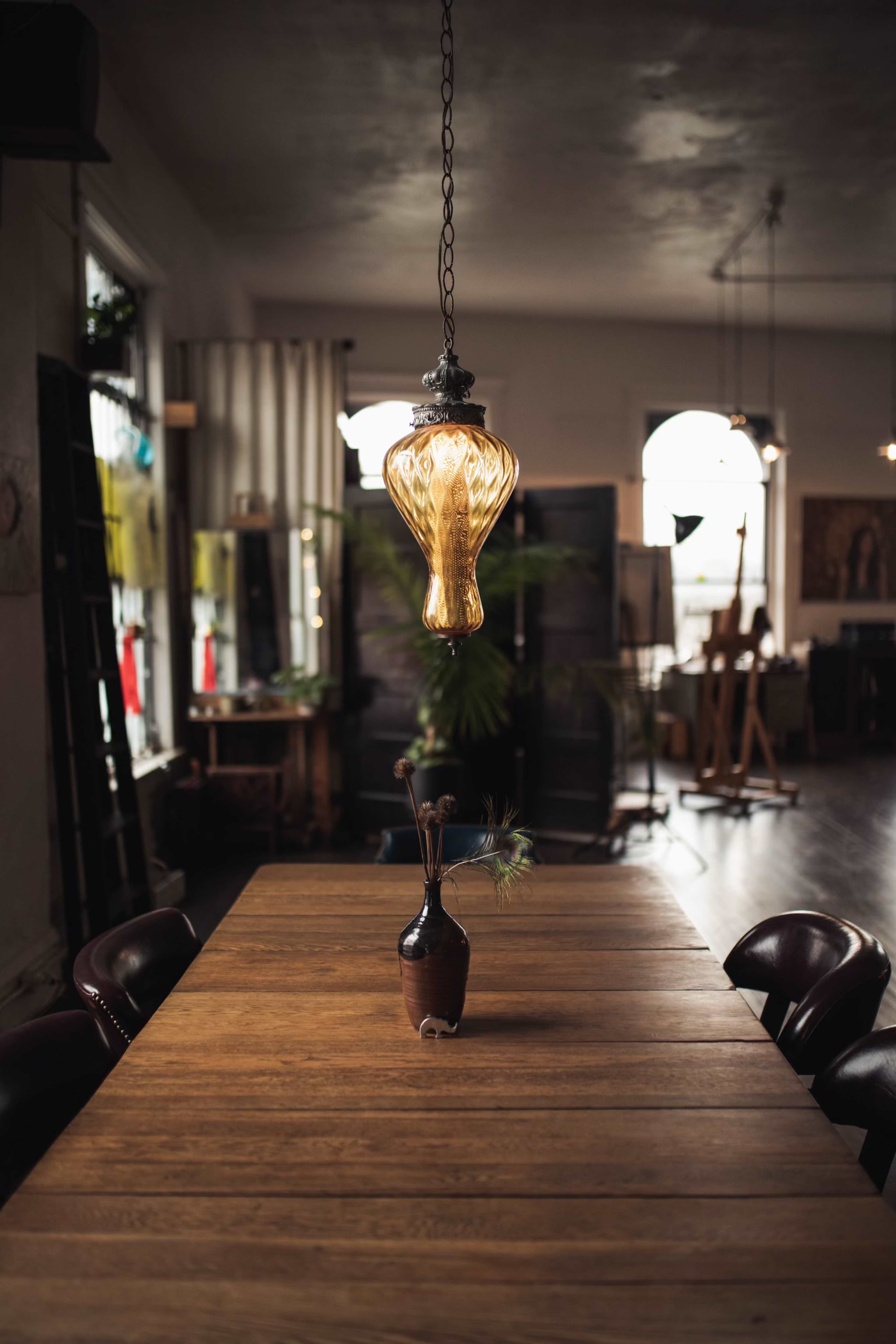 A pendant light hangs above a wooden dining table in a spacious room filled with natural light and art supplies.