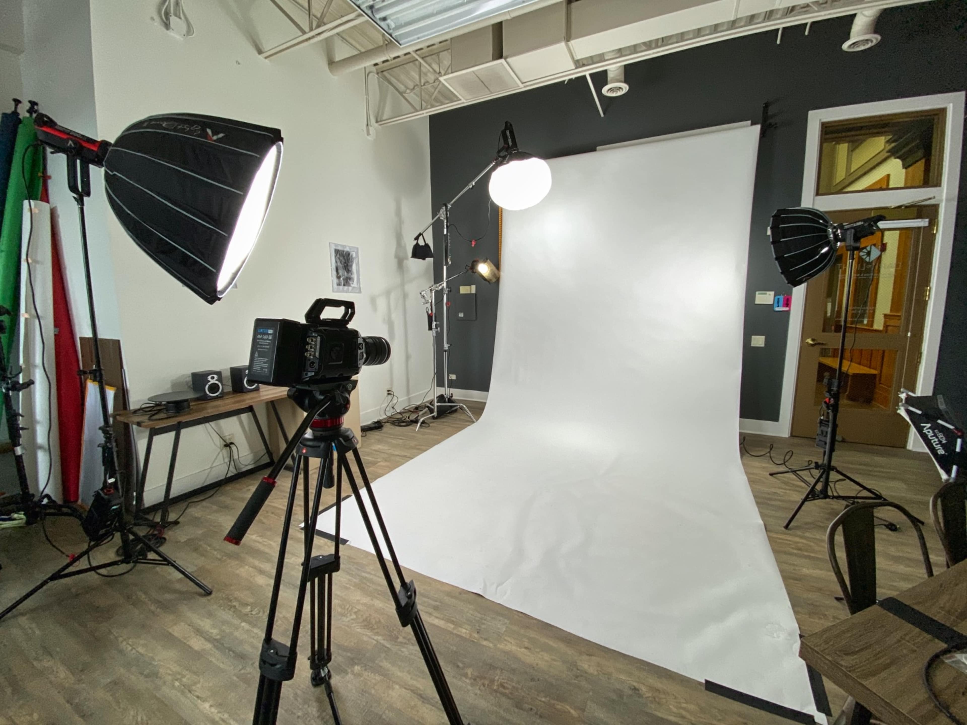 A photography studio features a white backdrop, a camera on a tripod, and multiple lighting setups.